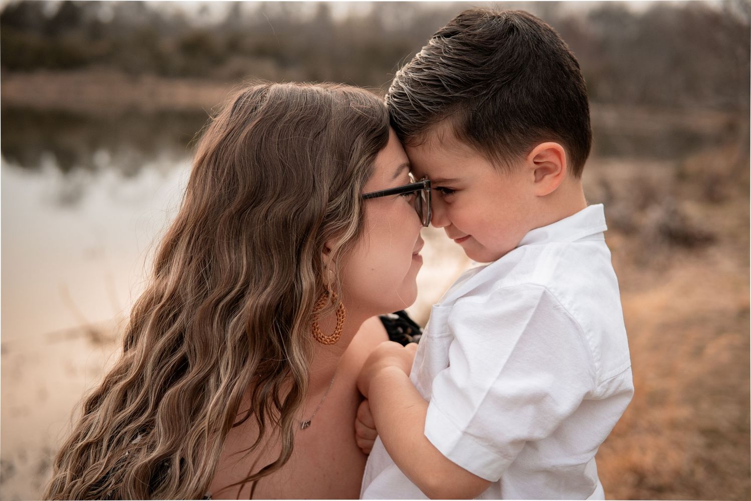 A tender moment shared between parent and child near a lake at sunset in a warm sepia-toned portrait.