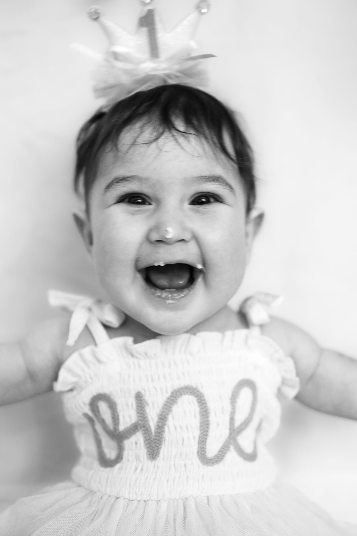 Black and white portrait of smiling baby in frilly dress.