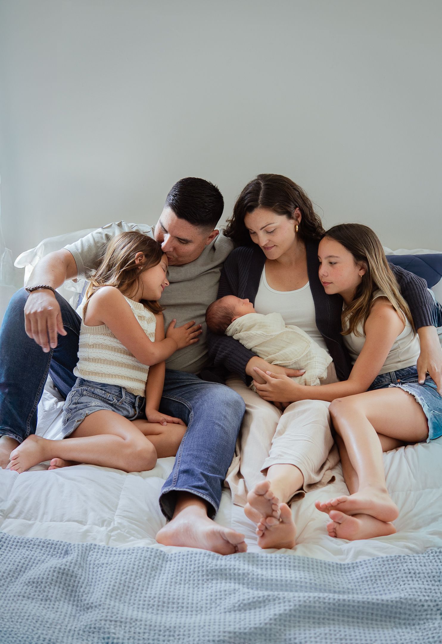 Family lying together on bed in tender moment with newborn during lifestyle photoshoot.