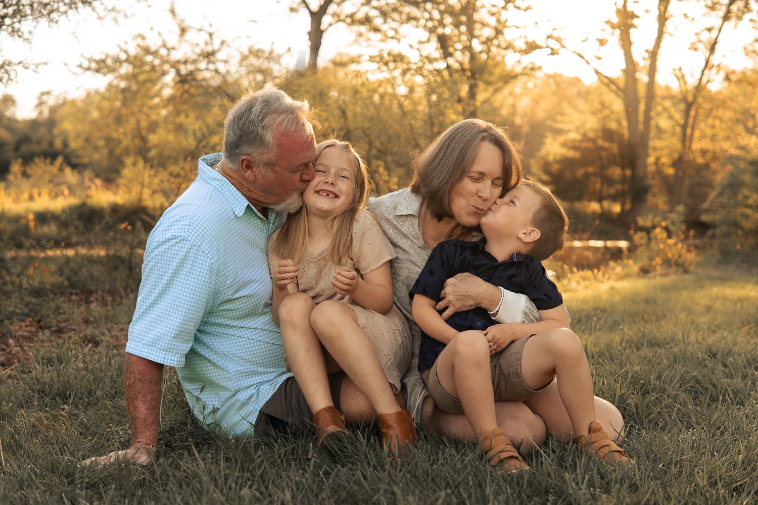 A family sits together on grass during golden hour sunset in a natural outdoor setting.