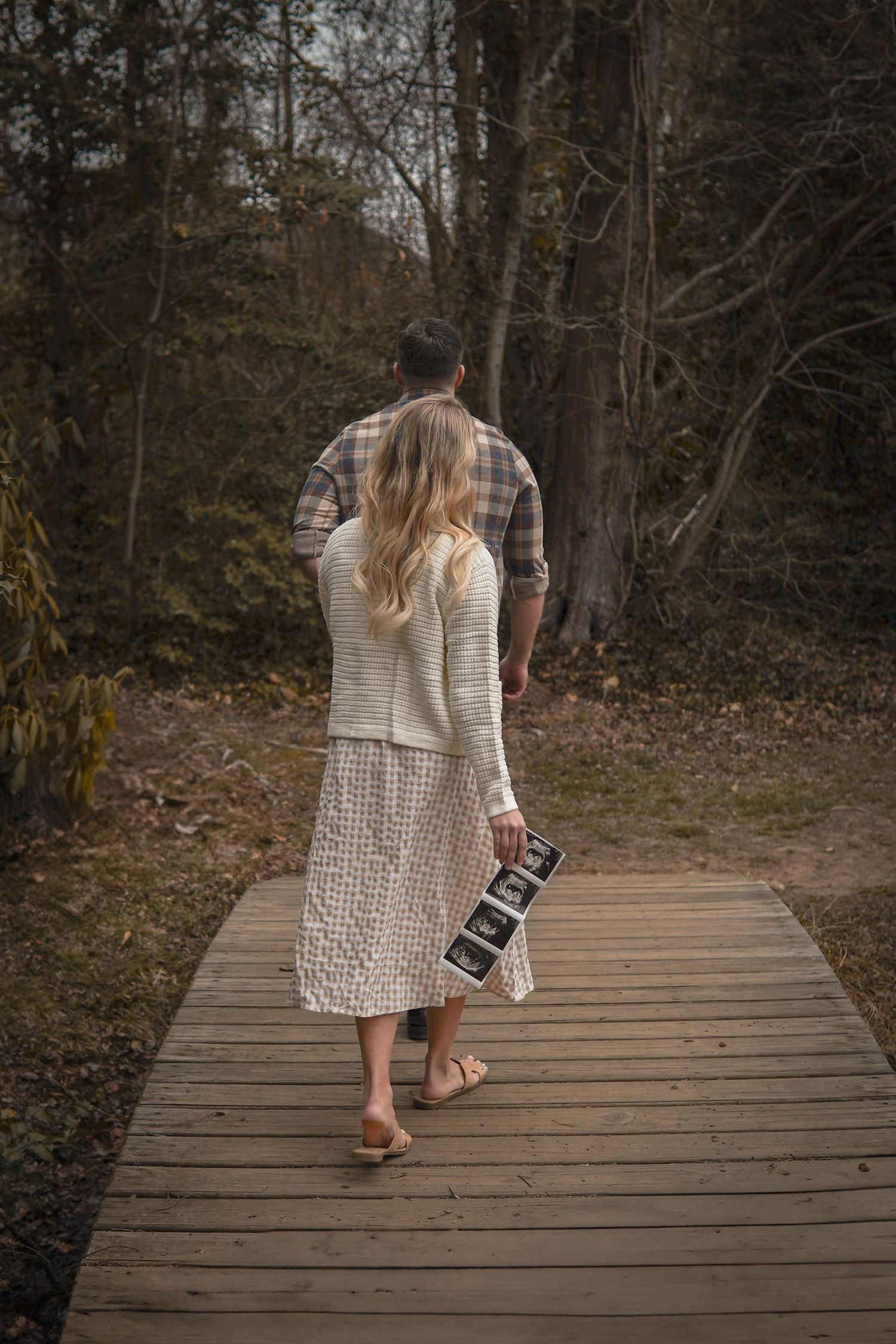 Couple walking together on a wooden boardwalk path through autumn woods while holding a vintage camera.