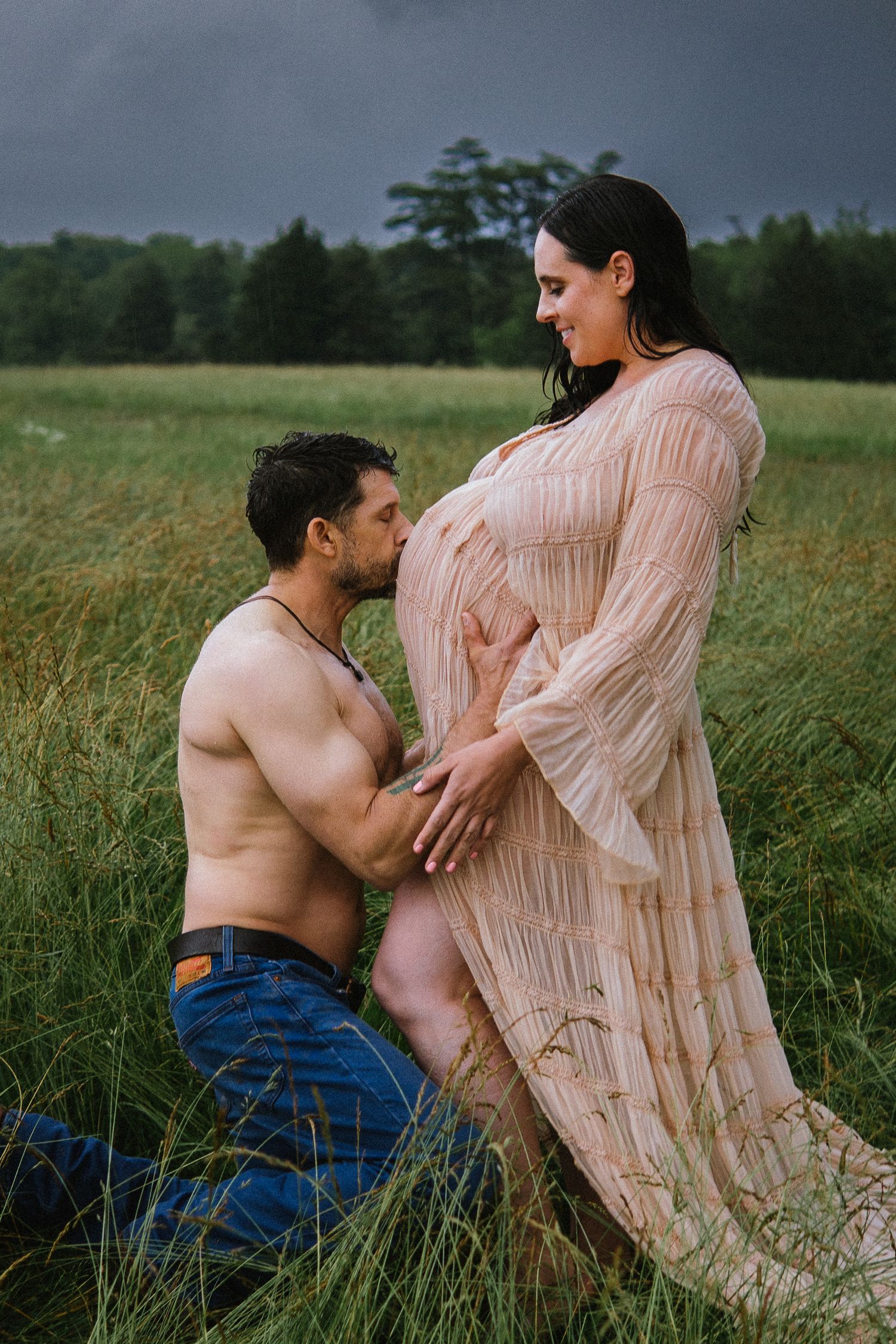 An artistic maternity photo captures a tender moment between a couple in a rustic field setting.