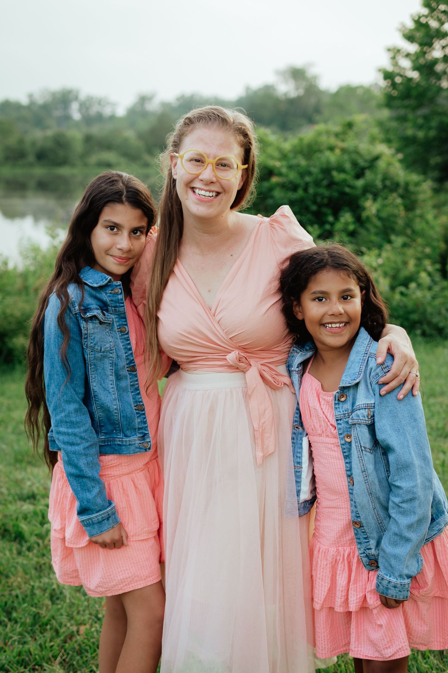 Three people in coordinated pink and denim outfits smiling together in an outdoor setting.
