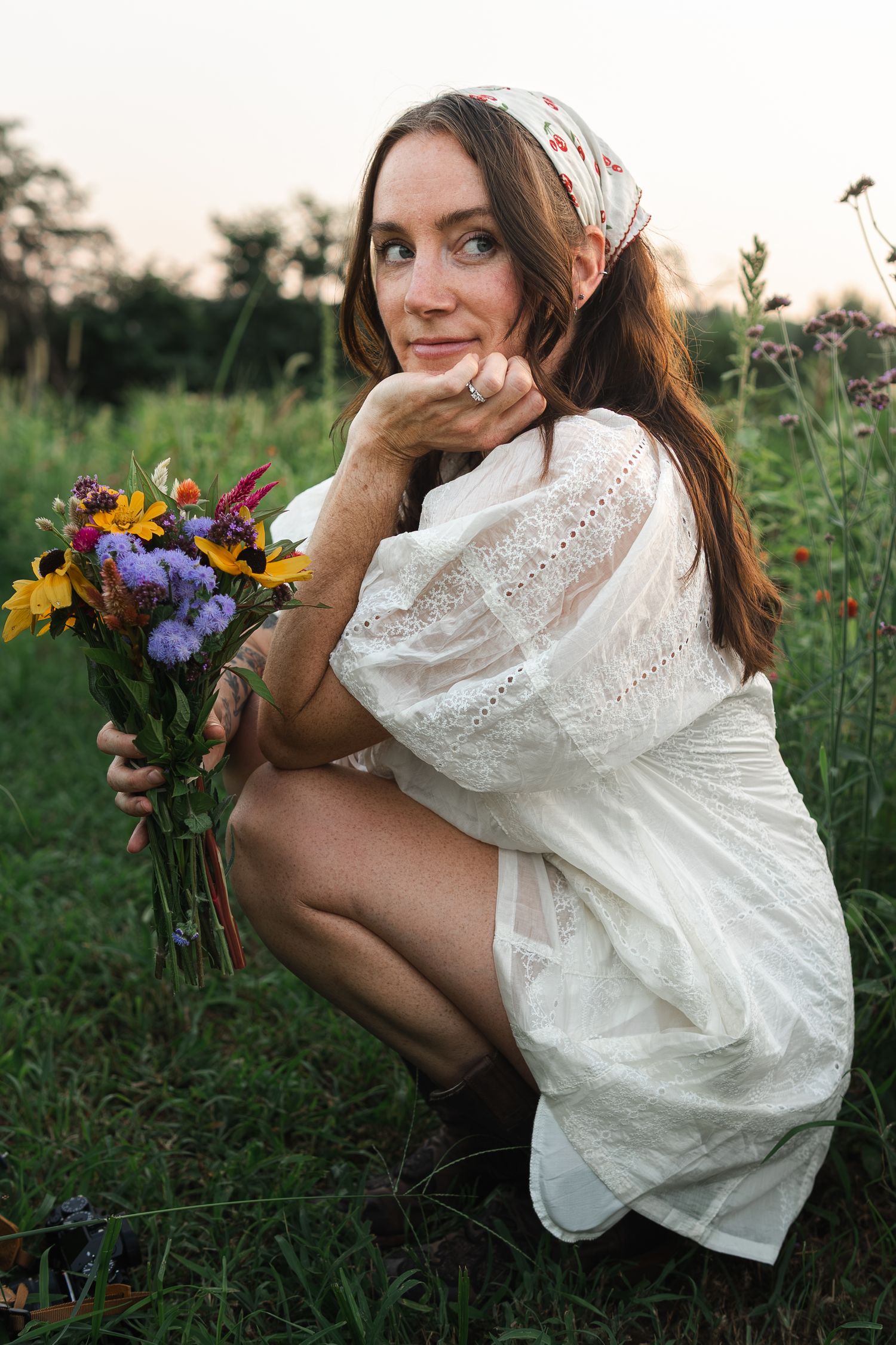 Person in white dress holds colorful wildflower bouquet while sitting in summer meadow.