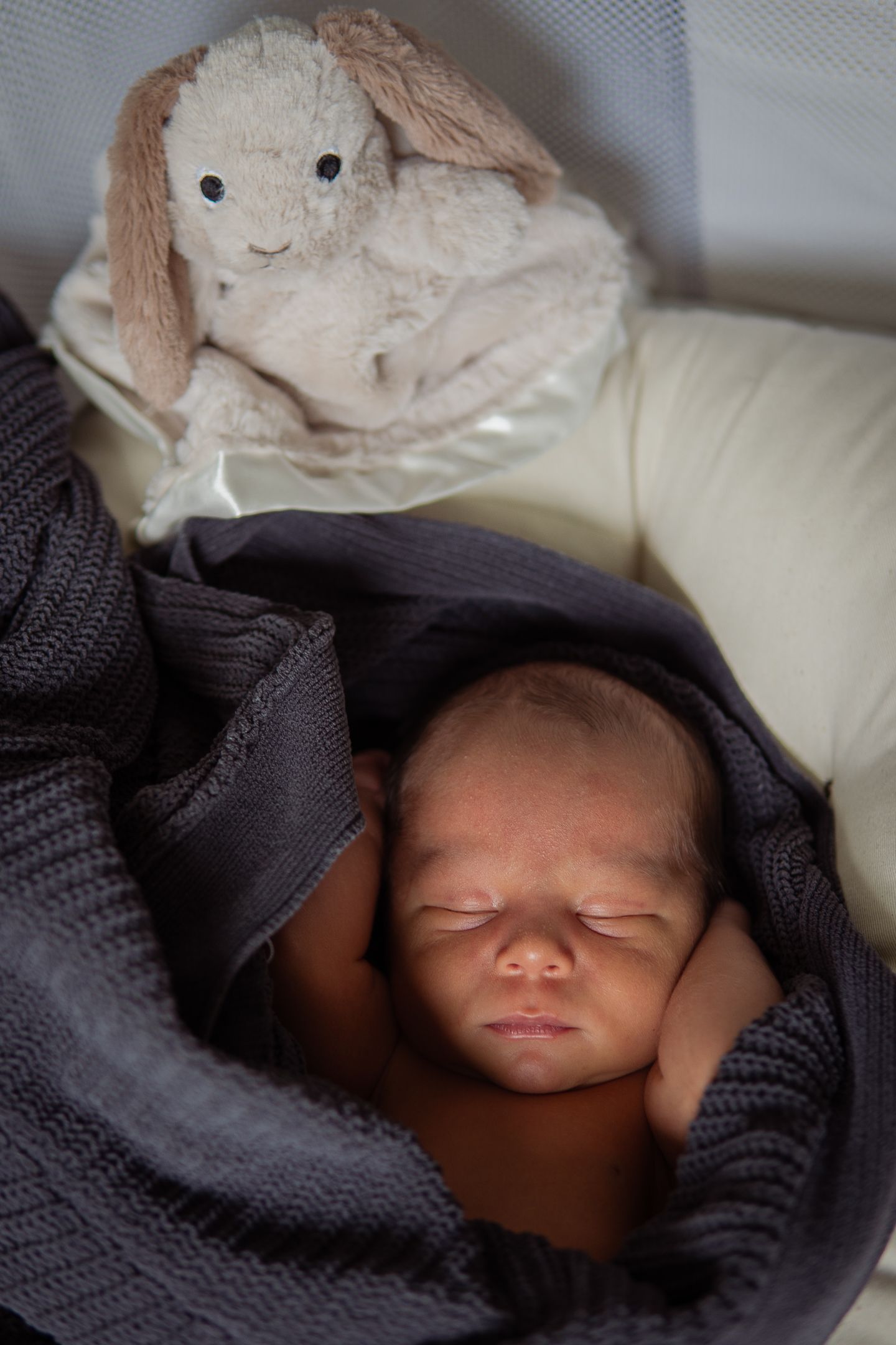 A sleeping newborn baby wrapped in a dark knit blanket.