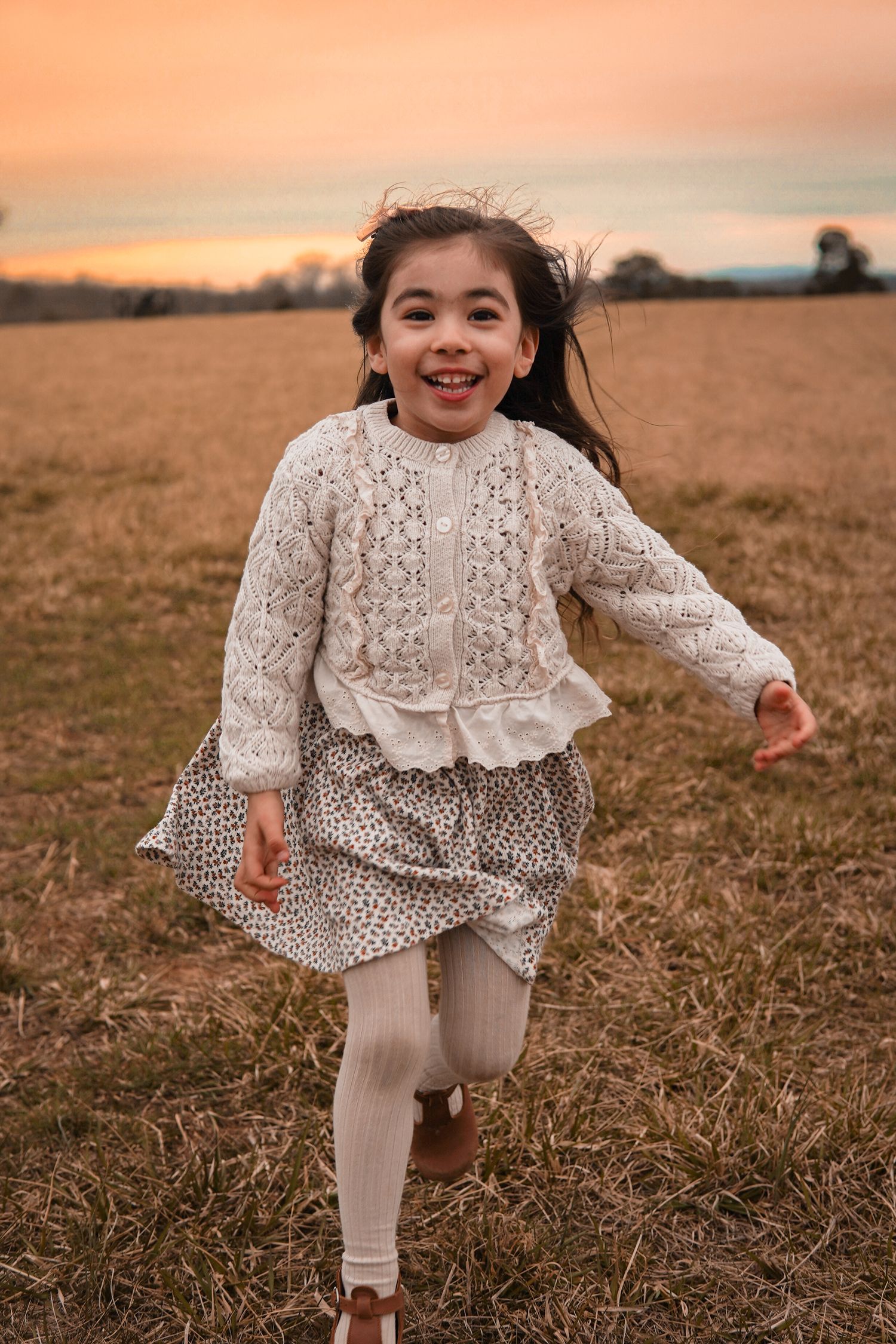 Series of photos showing a young child playing in a field wearing a white vintage-style lace dress and white tights.
