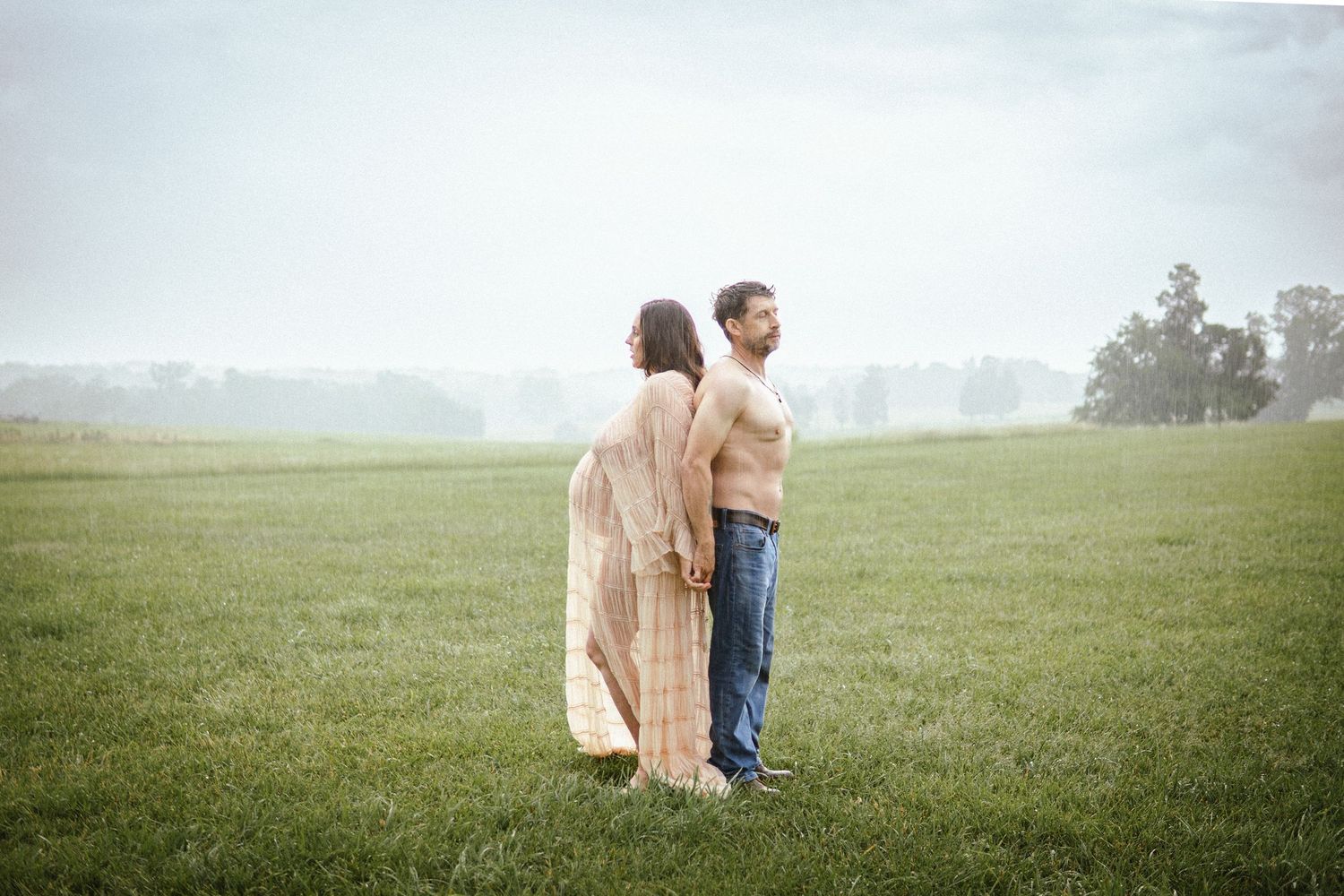 A couple sitting close together on green grass in a misty field during a romantic outdoor photo session.