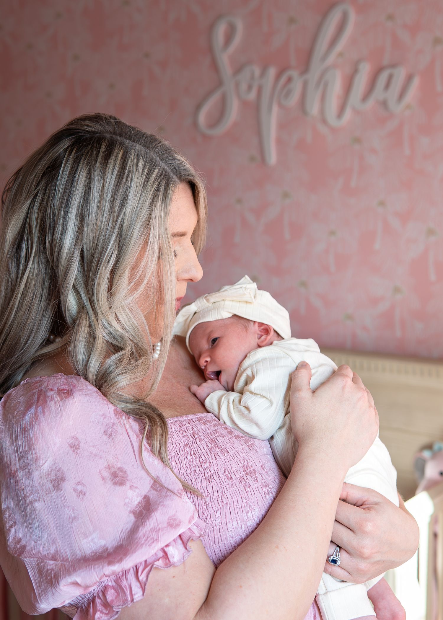 A tender moment between a mother in pink and her newborn baby in a soft white blanket.