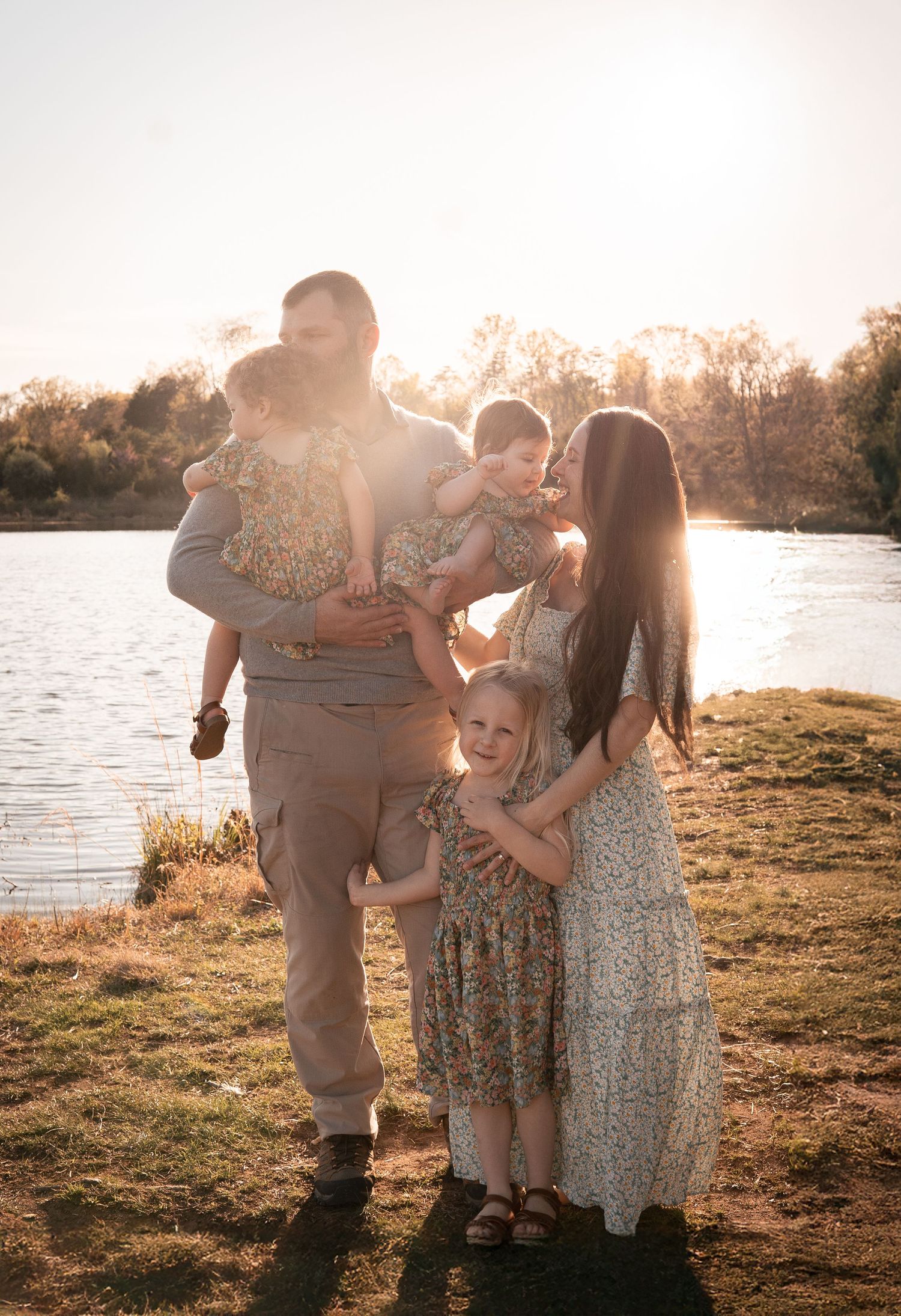 A family of five poses together at sunset by a lake, backlit by warm golden light in Haymarket, Virginia.