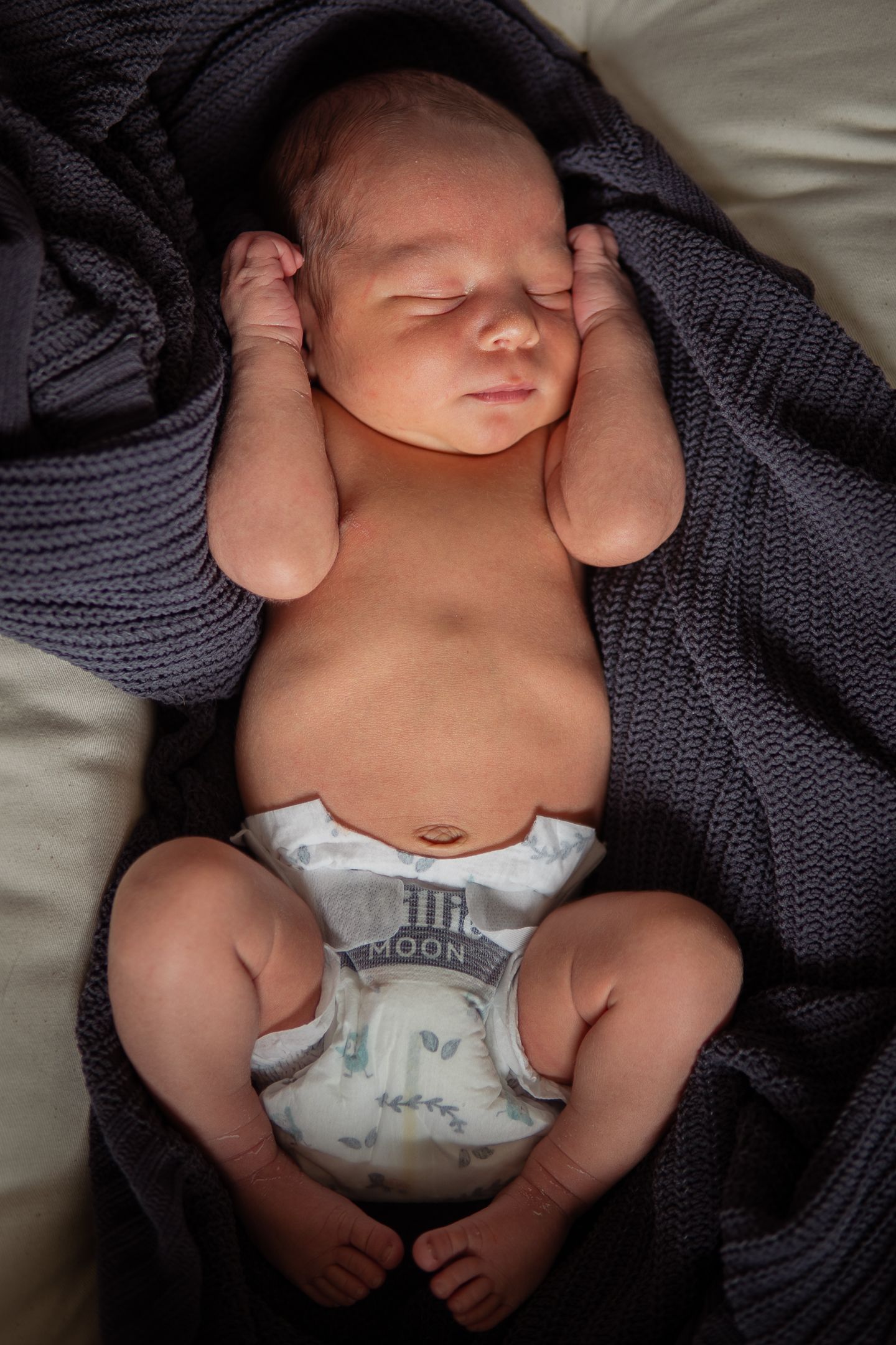 Sleeping newborn wearing diaper nestled in soft gray knit blanket.