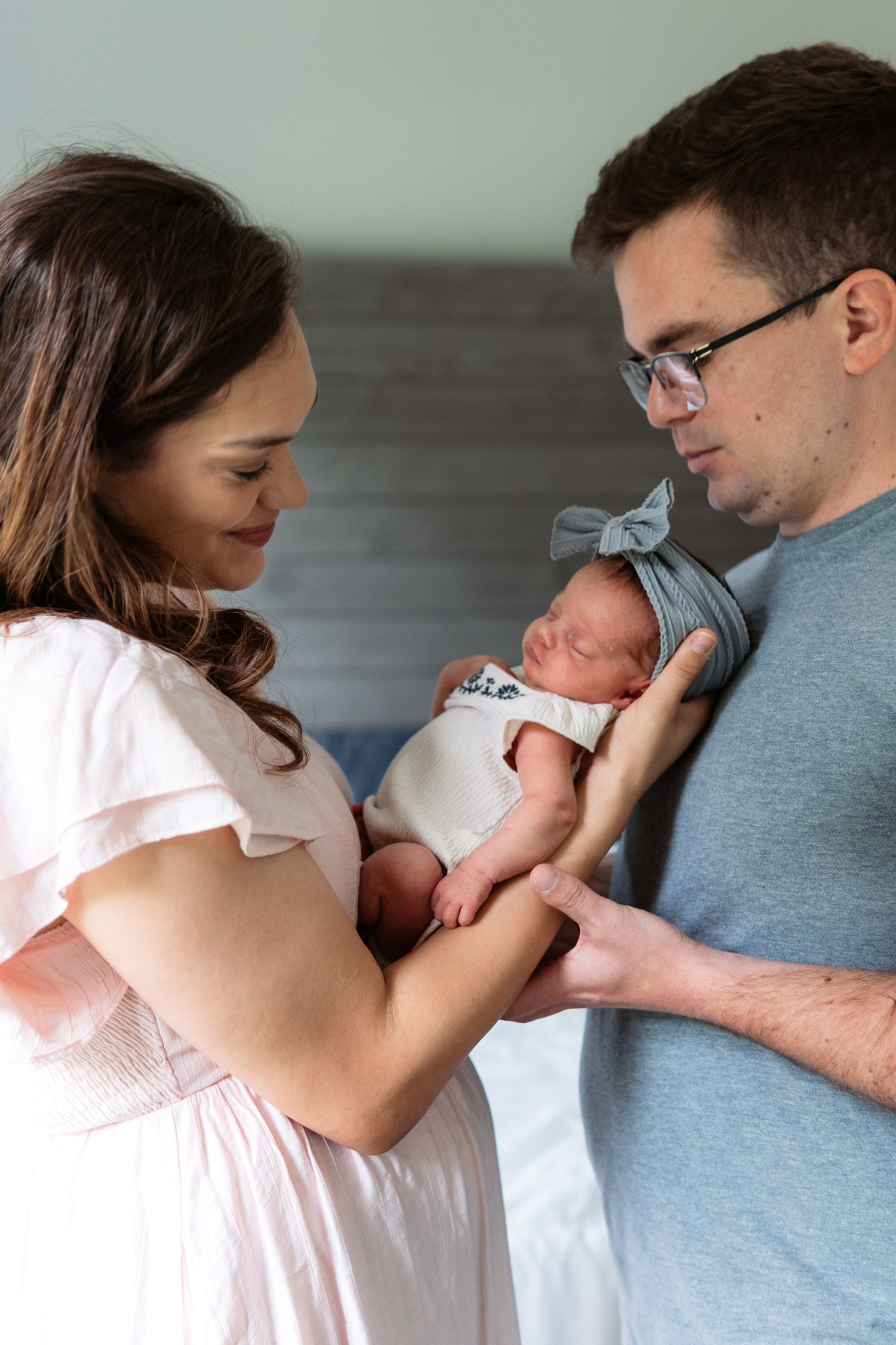 Parents in casual attire tenderly holding and gazing at their newborn baby.