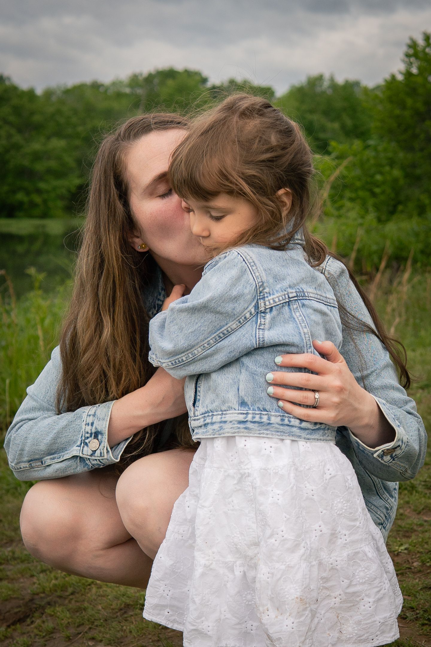 A series of tender embraces between parent and child in a natural outdoor setting wearing denim and white.