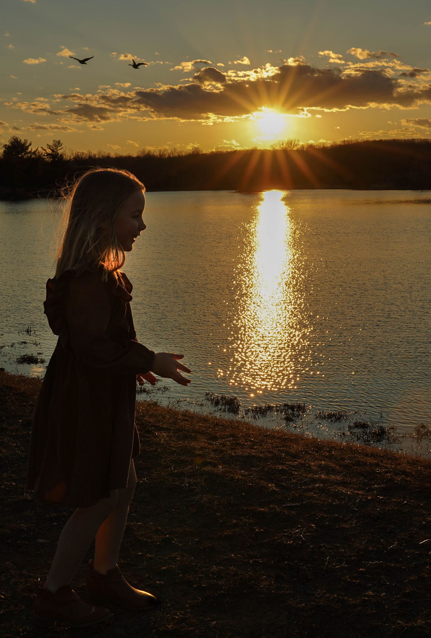 A silhouette stands by a tranquil lake at sunset, with golden light reflecting off the water and clouds in the sky.