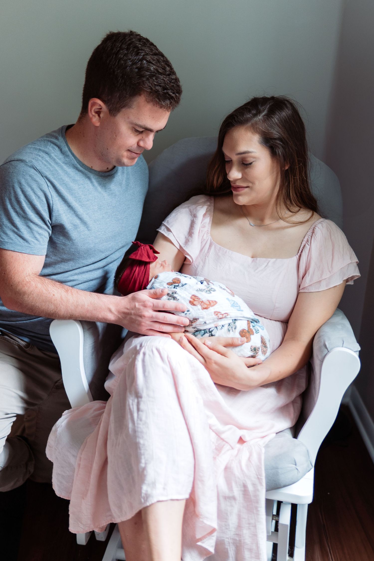 A tender family moment as parents cradle their newborn baby wrapped in a floral swaddle blanket.
