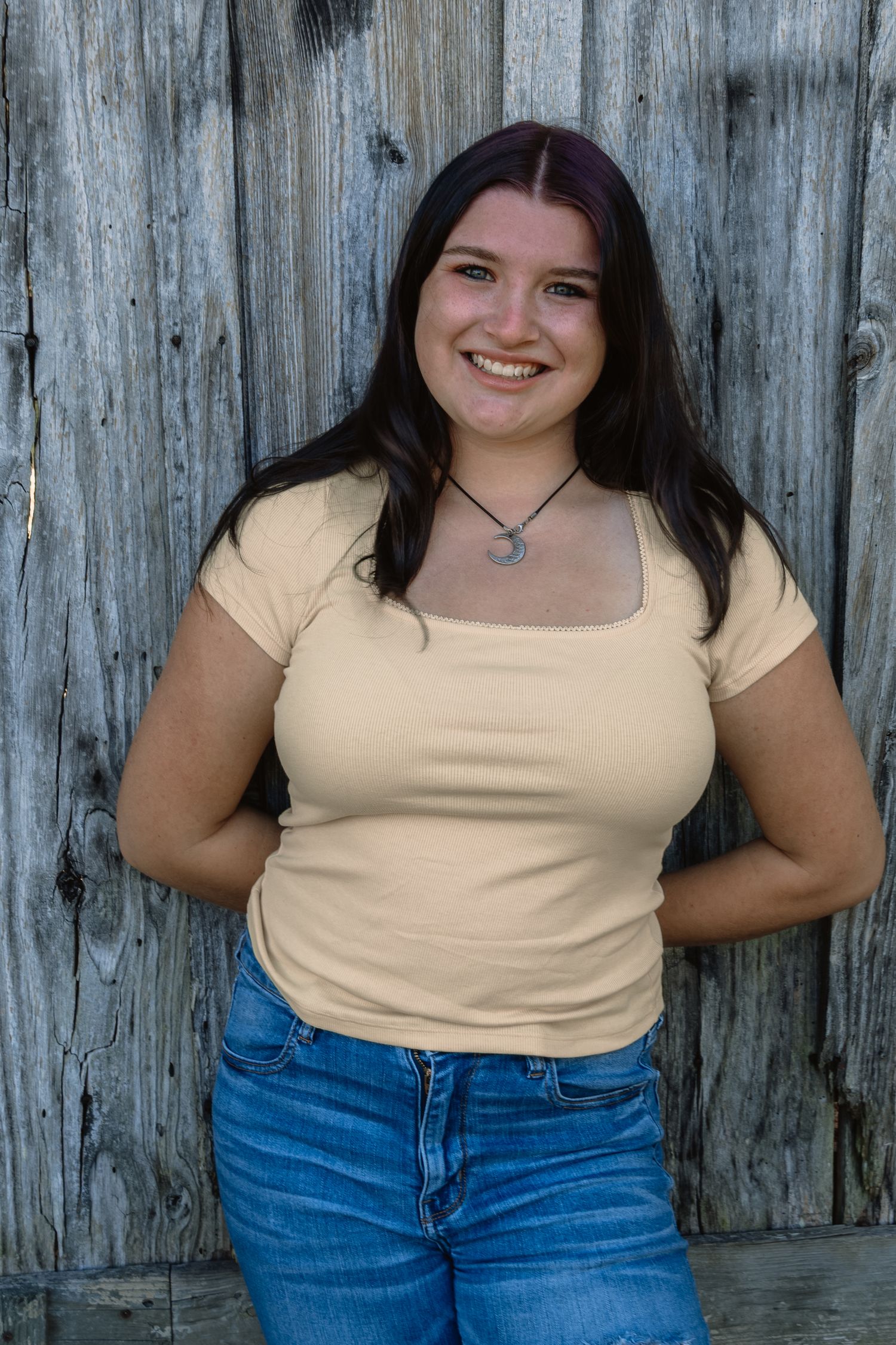 Person in yellow t-shirt and blue jeans poses against wooden fence in casual outdoor portrait series.
