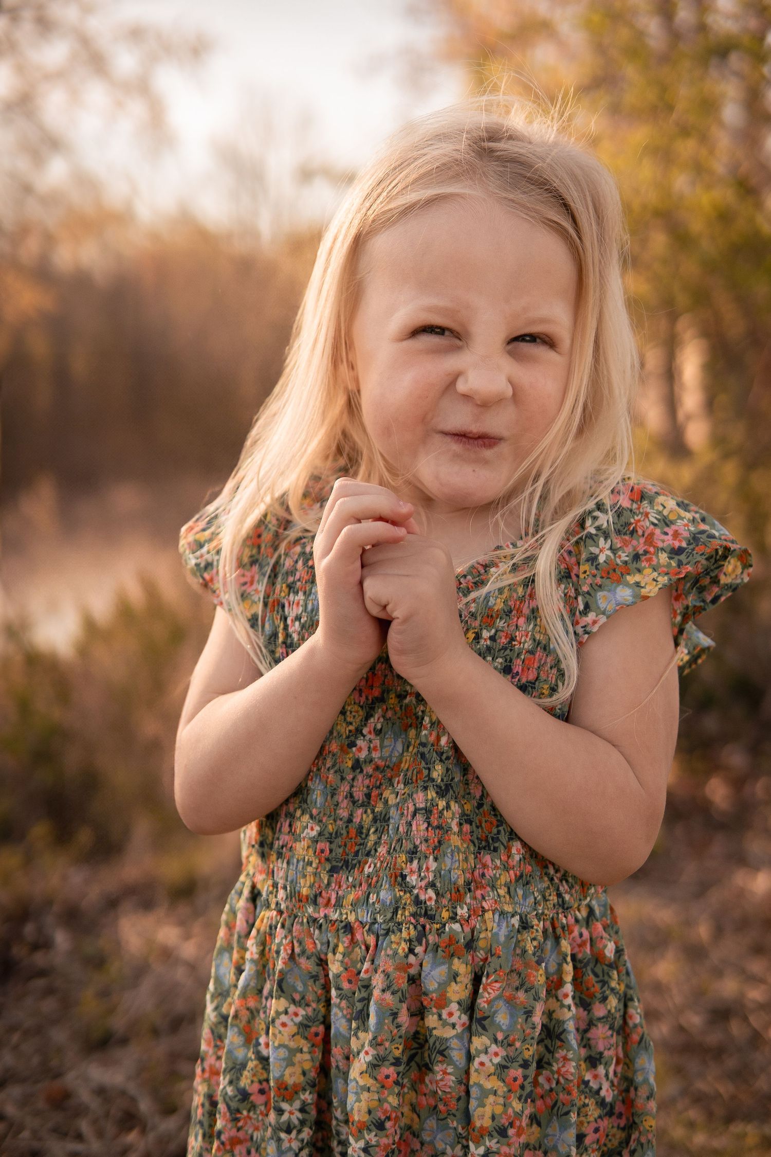 Sweet outdoor portrait in floral dress against autumn backdrop with warm golden sunlight filtering through trees in Haymarket, Virginia.