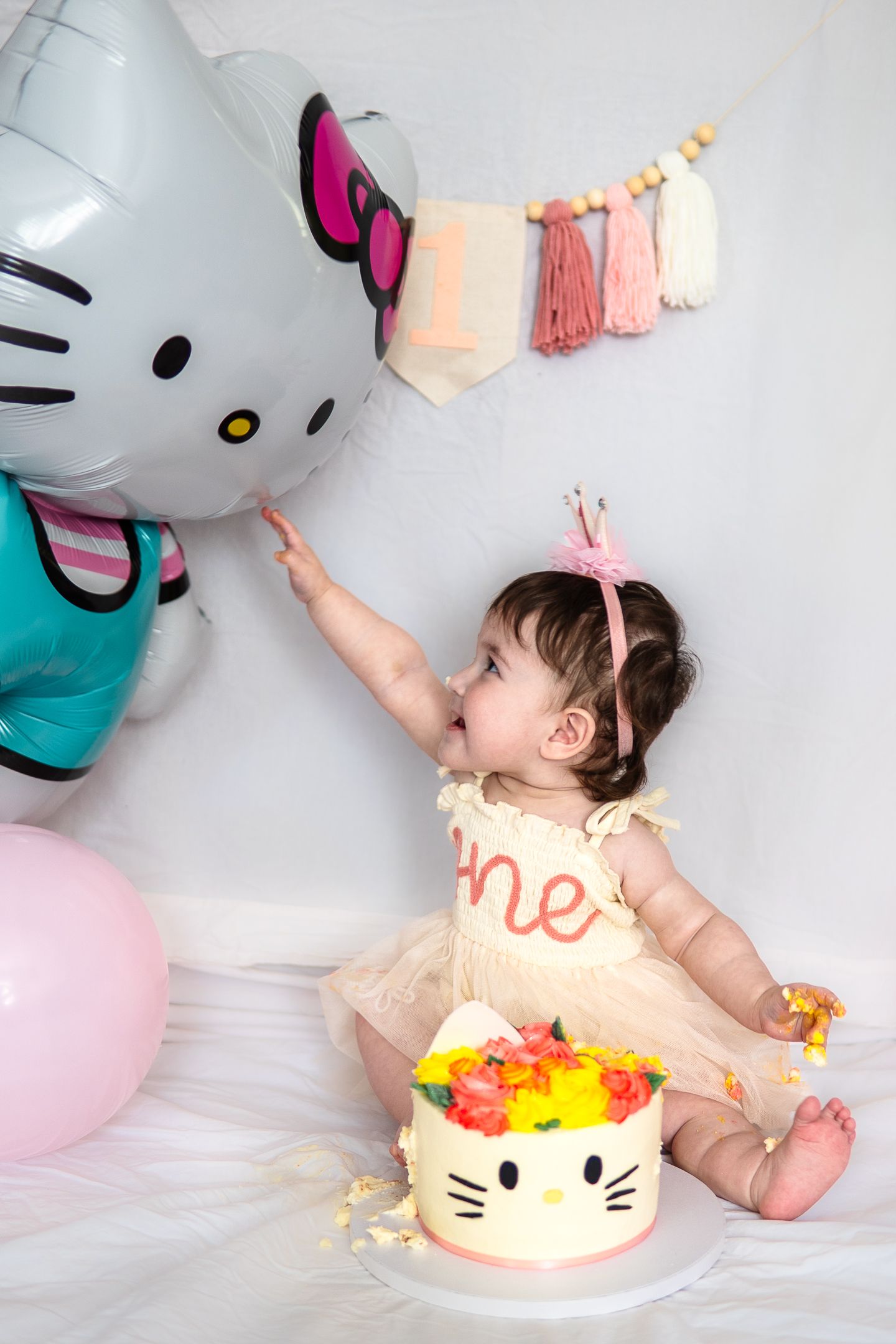 Baby reaching for Hello Kitty decorations during cake smash photo session.