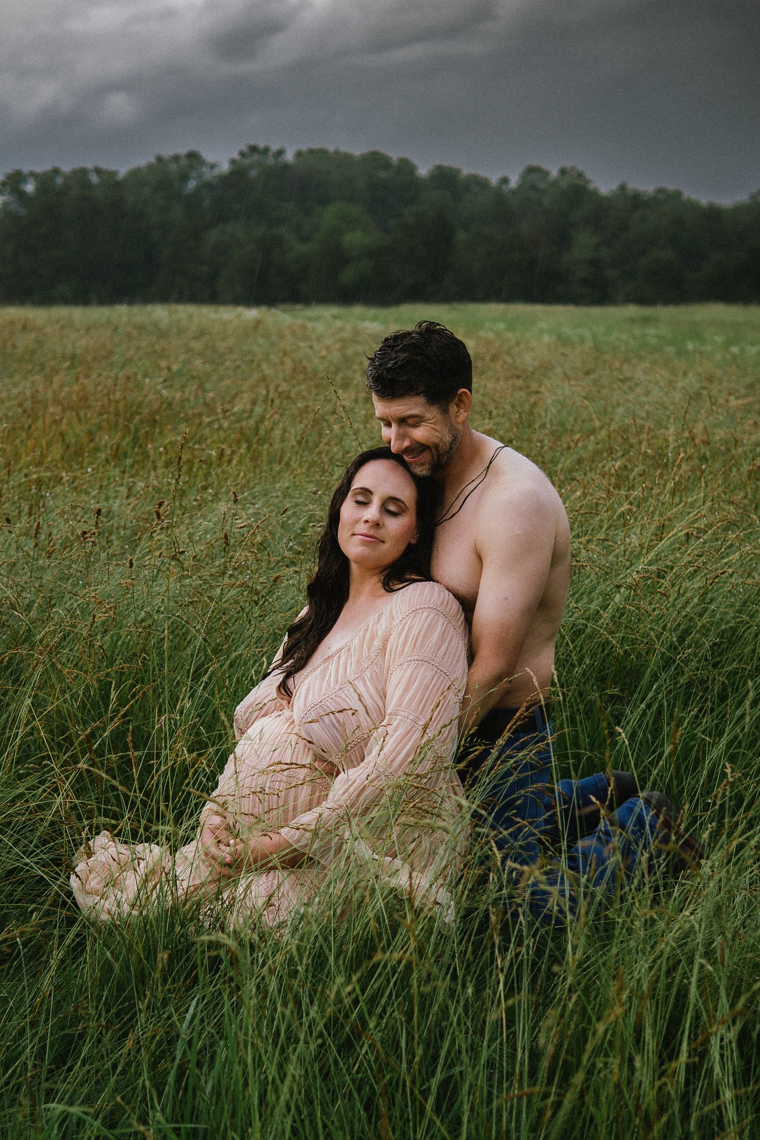 A romantic maternity photo shoot in tall grass with a couple laying together in nature.