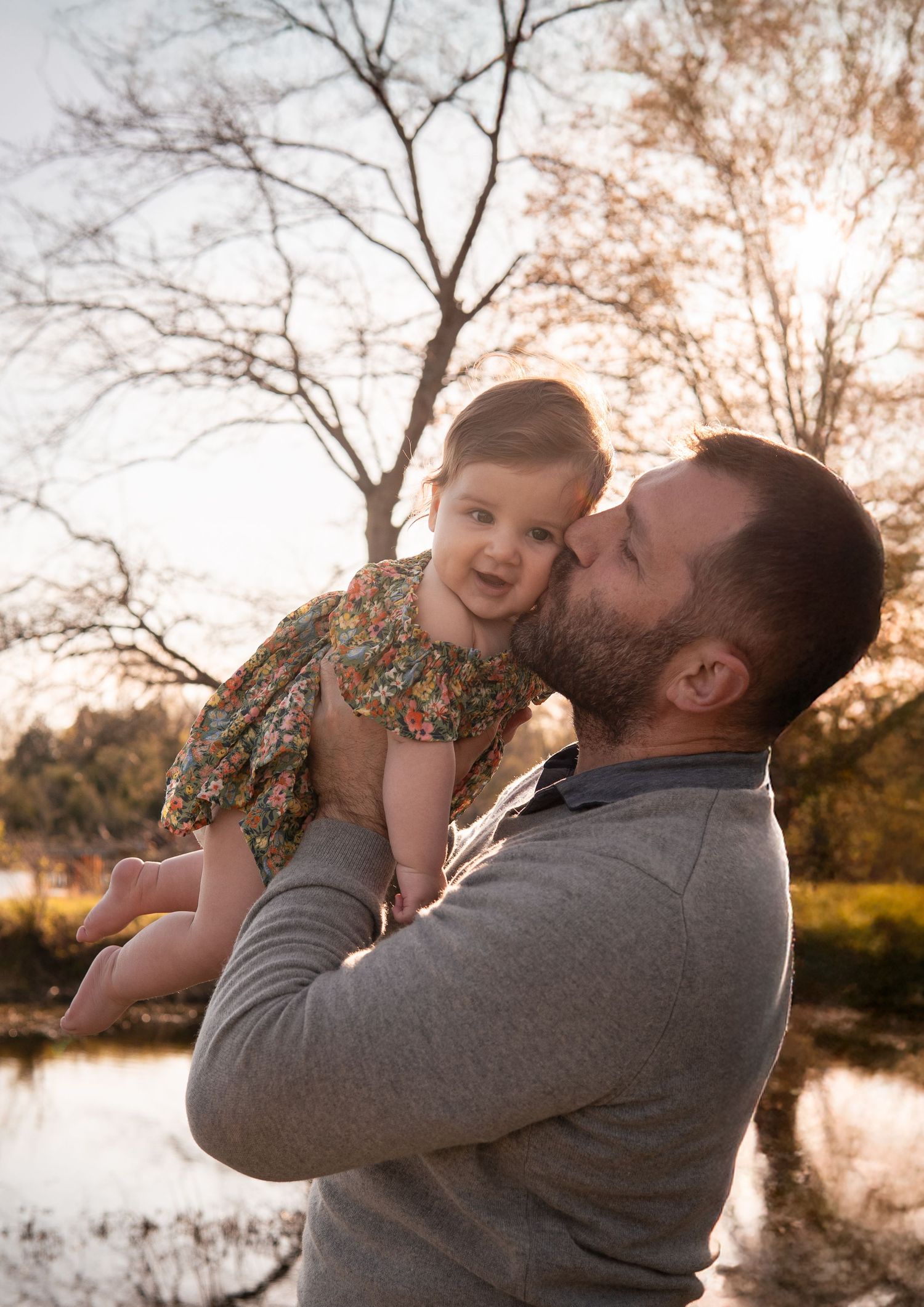 A tender moment captured at sunset by a lake with bare trees in the background.