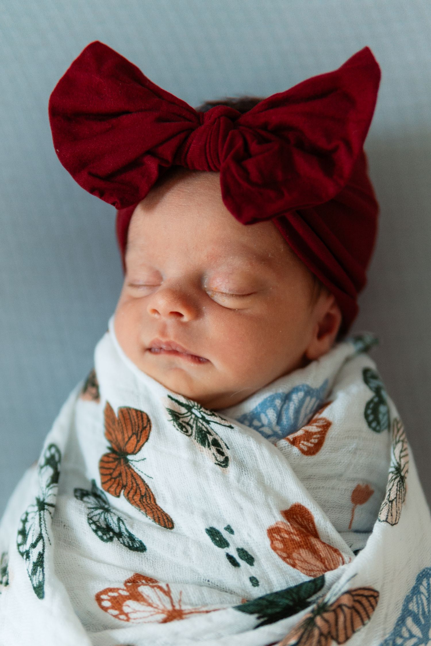 Sleeping newborn wrapped in butterfly print swaddle with red bow headband.