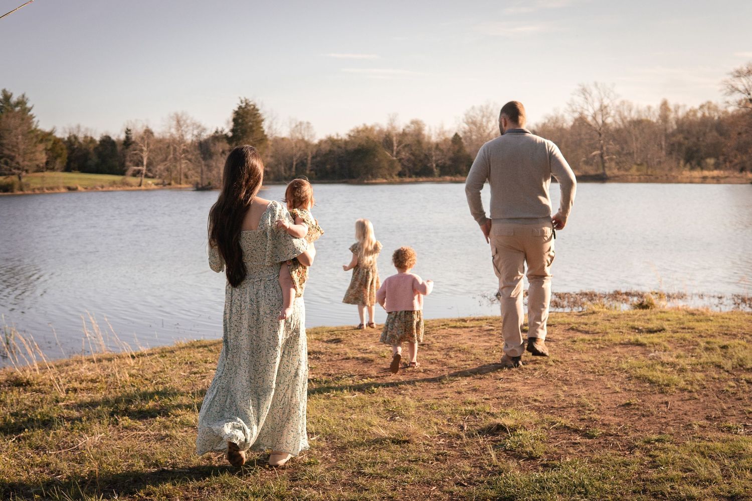 A family walks together along a peaceful lakeside trail during golden hour at sunset.