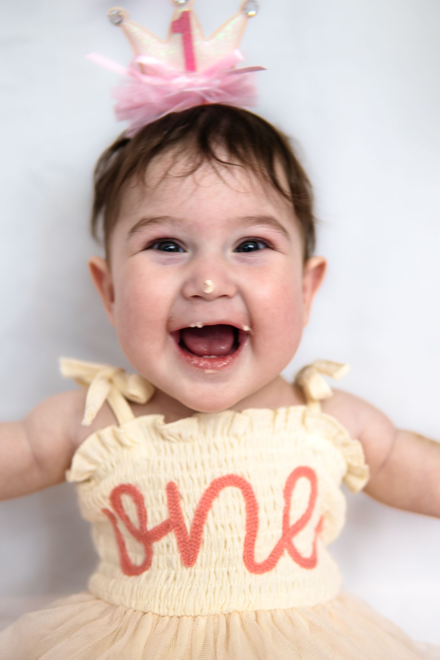 A joyful first birthday celebration featuring a light yellow tulle dress with 'one' text and a pink crown accessory.