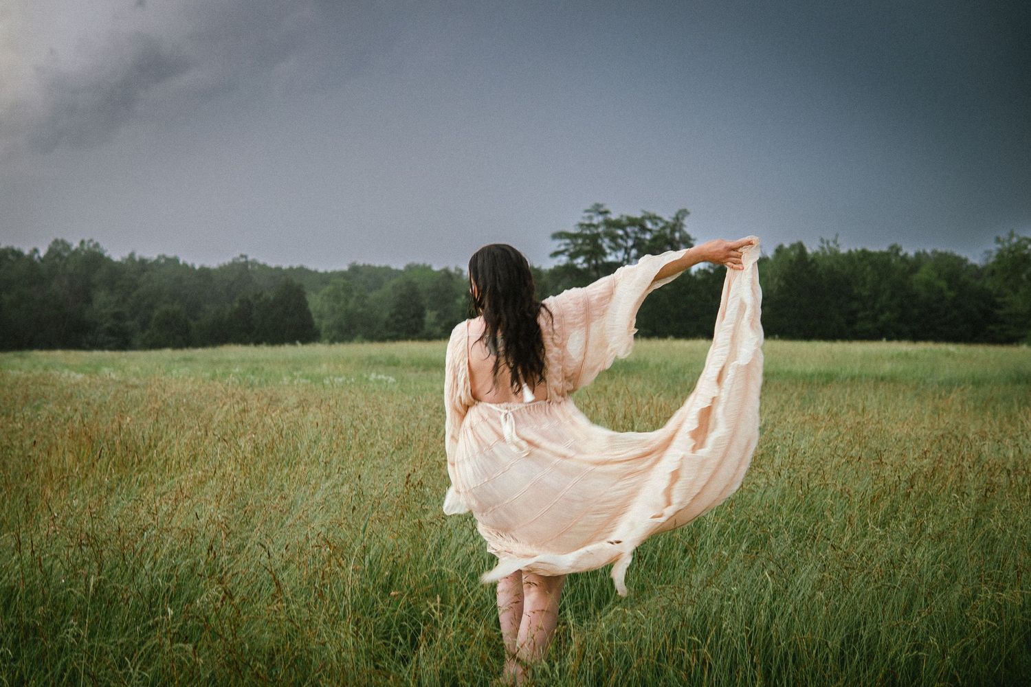 A flowing pink fabric billows gracefully across a green grassy field against a moody overcast sky.