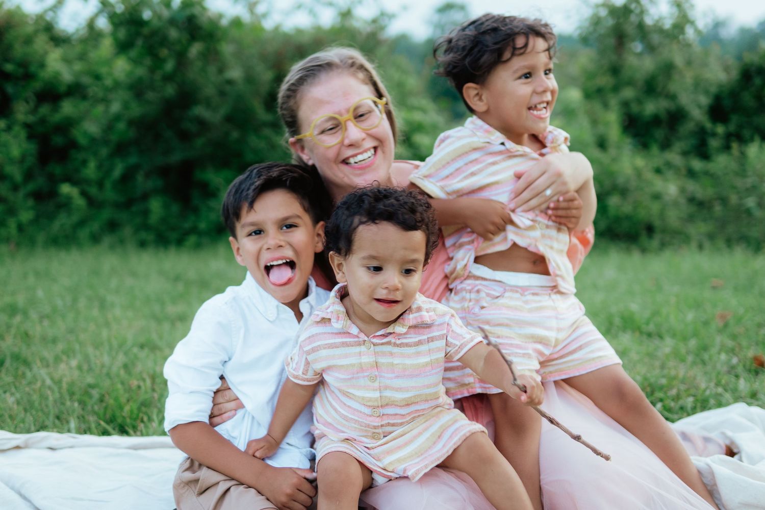 Family sitting together on blanket having fun outdoors in green summer field.