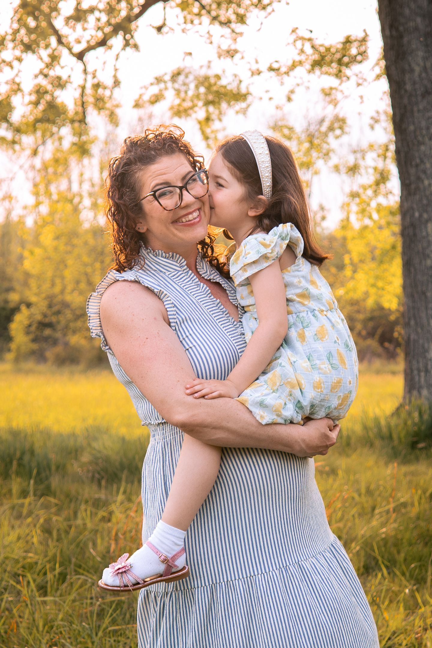 Two people embracing in a warm sunset glow among autumn trees wearing striped and floral dresses with white accessories.