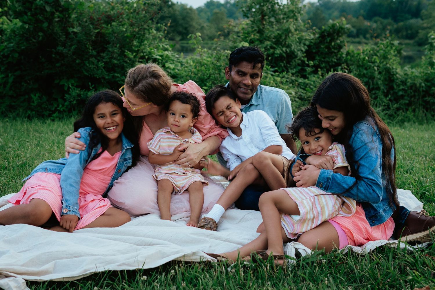 A family cuddles together on a blanket in the grass during an outdoor photo session.
