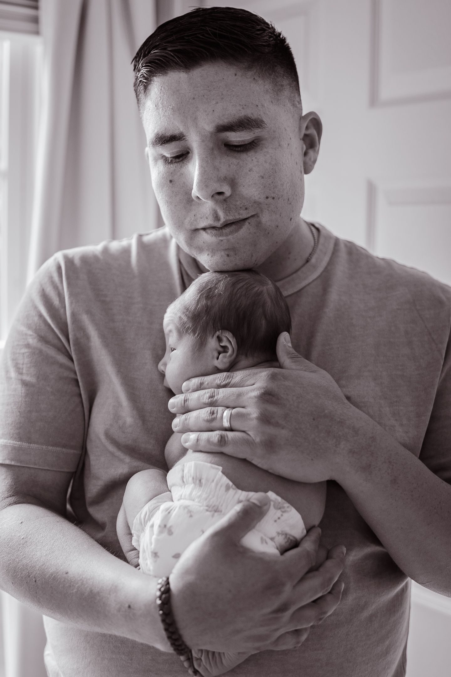 Sweet interaction between a newborn and someone wearing a grey sweatshirt in a bright room.