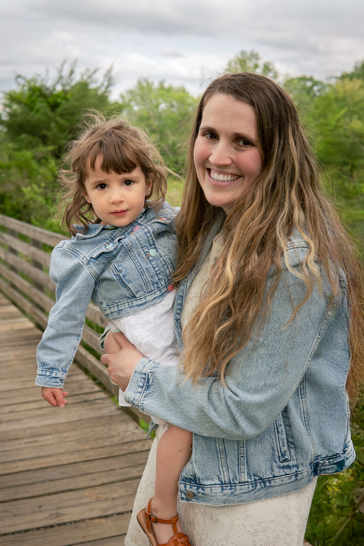 Parent and child share tender moments while wearing coordinating denim outfits on a wooden bridge.