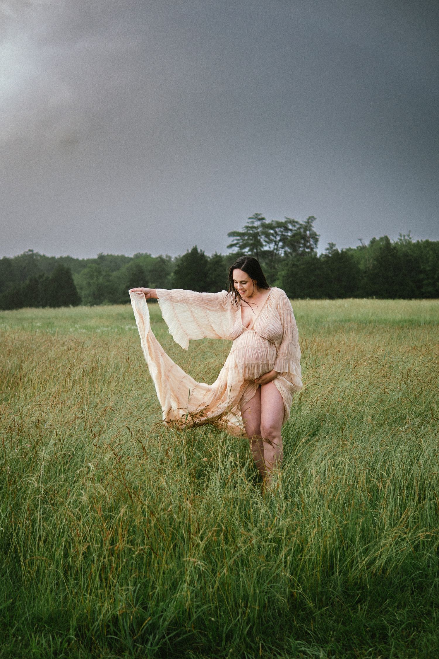 A dreamy maternity shoot captures movement of a flowy peach dress in a sun-lit meadow.