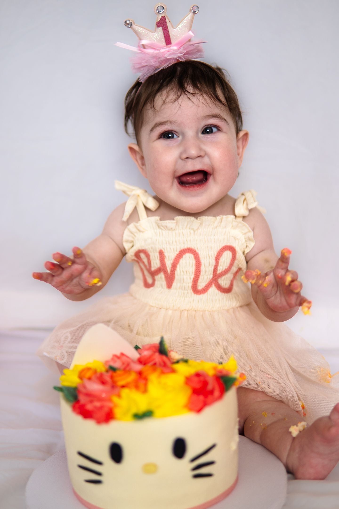 First birthday celebration featuring a colorful floral cake with cat whiskers and festive pink crown decoration.