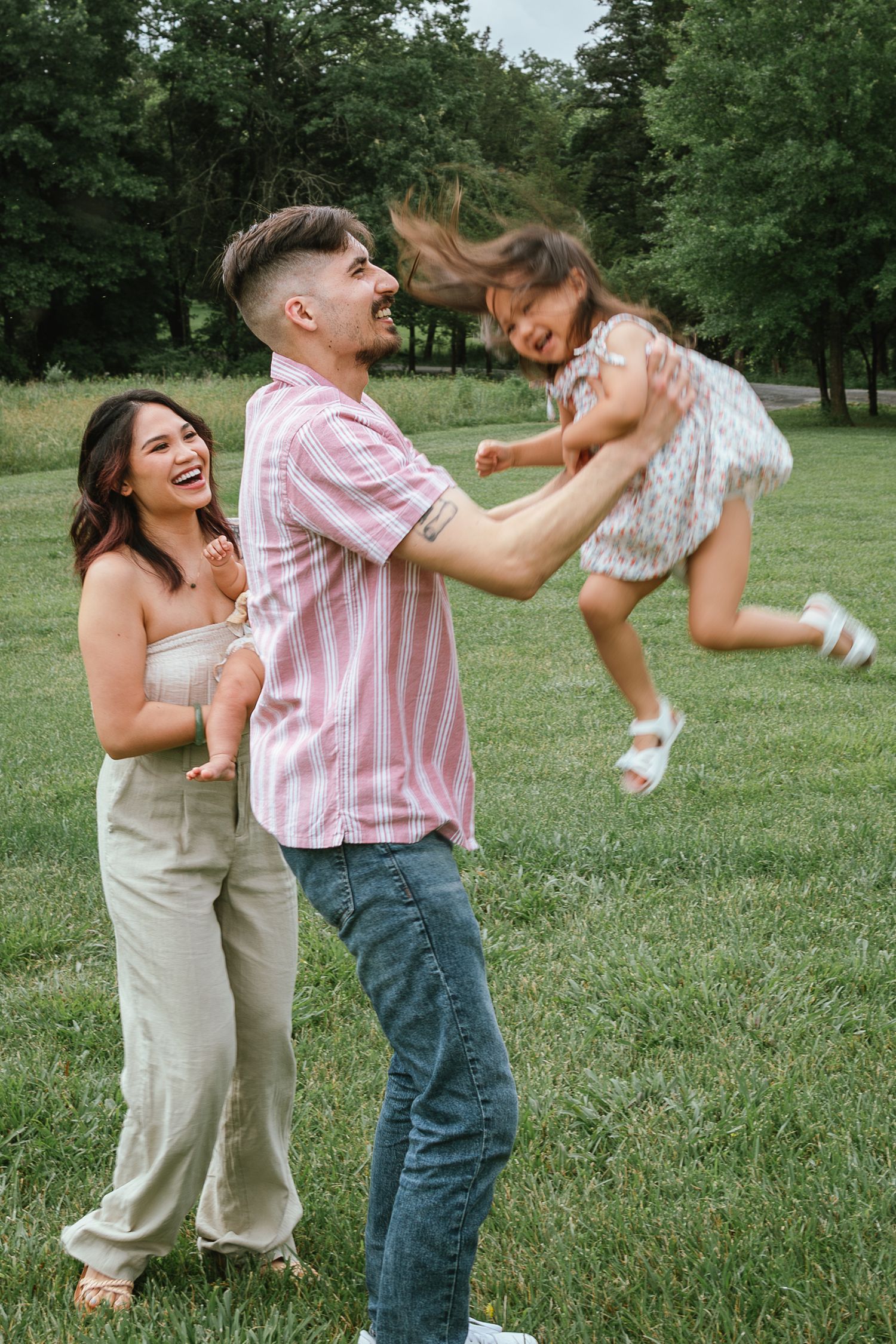 A playful family moment on a grassy field with a pink striped shirt and khaki outfit.