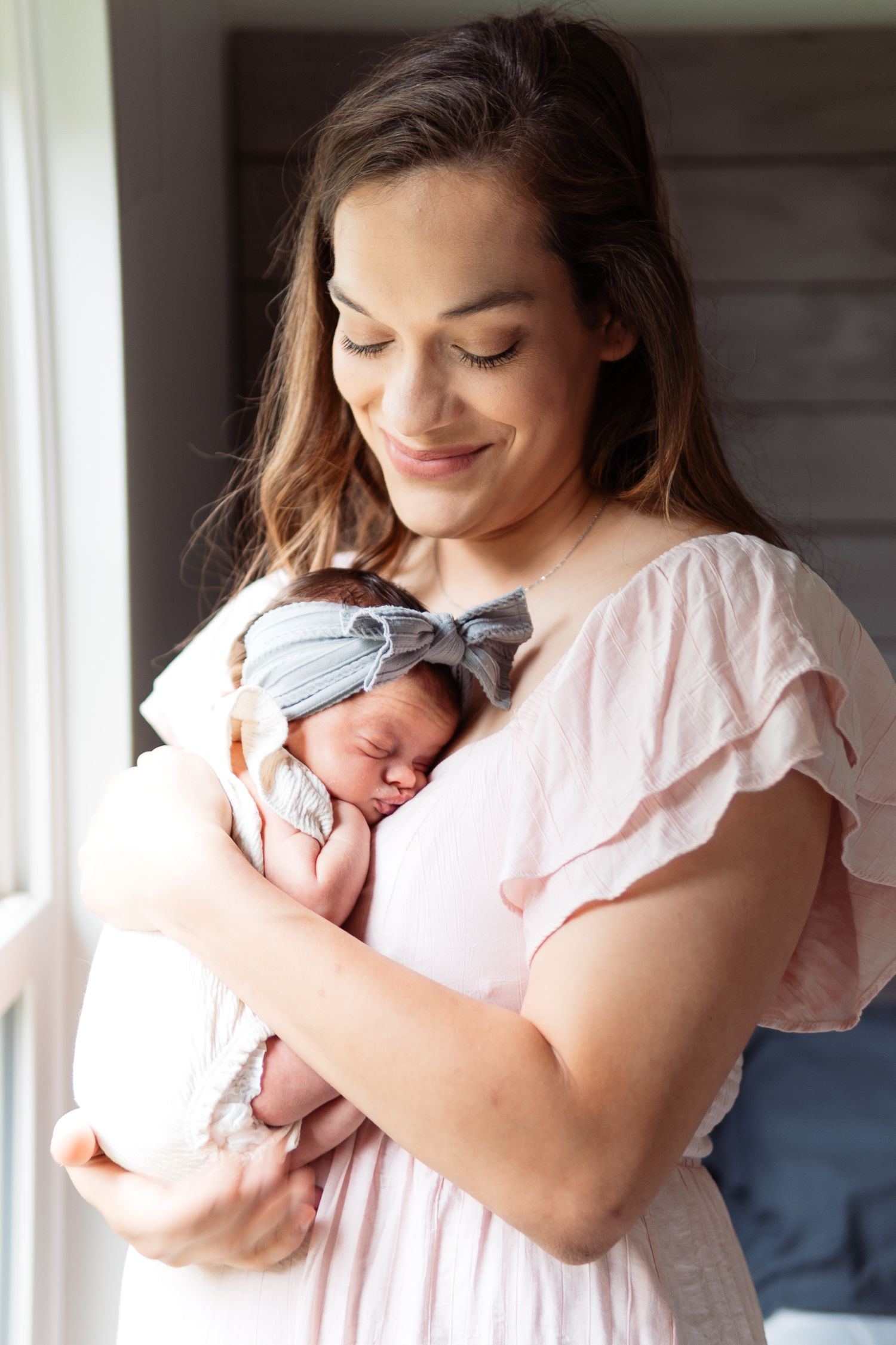 New parents share tender moments with their newborn baby in a series of intimate portraits by a window.