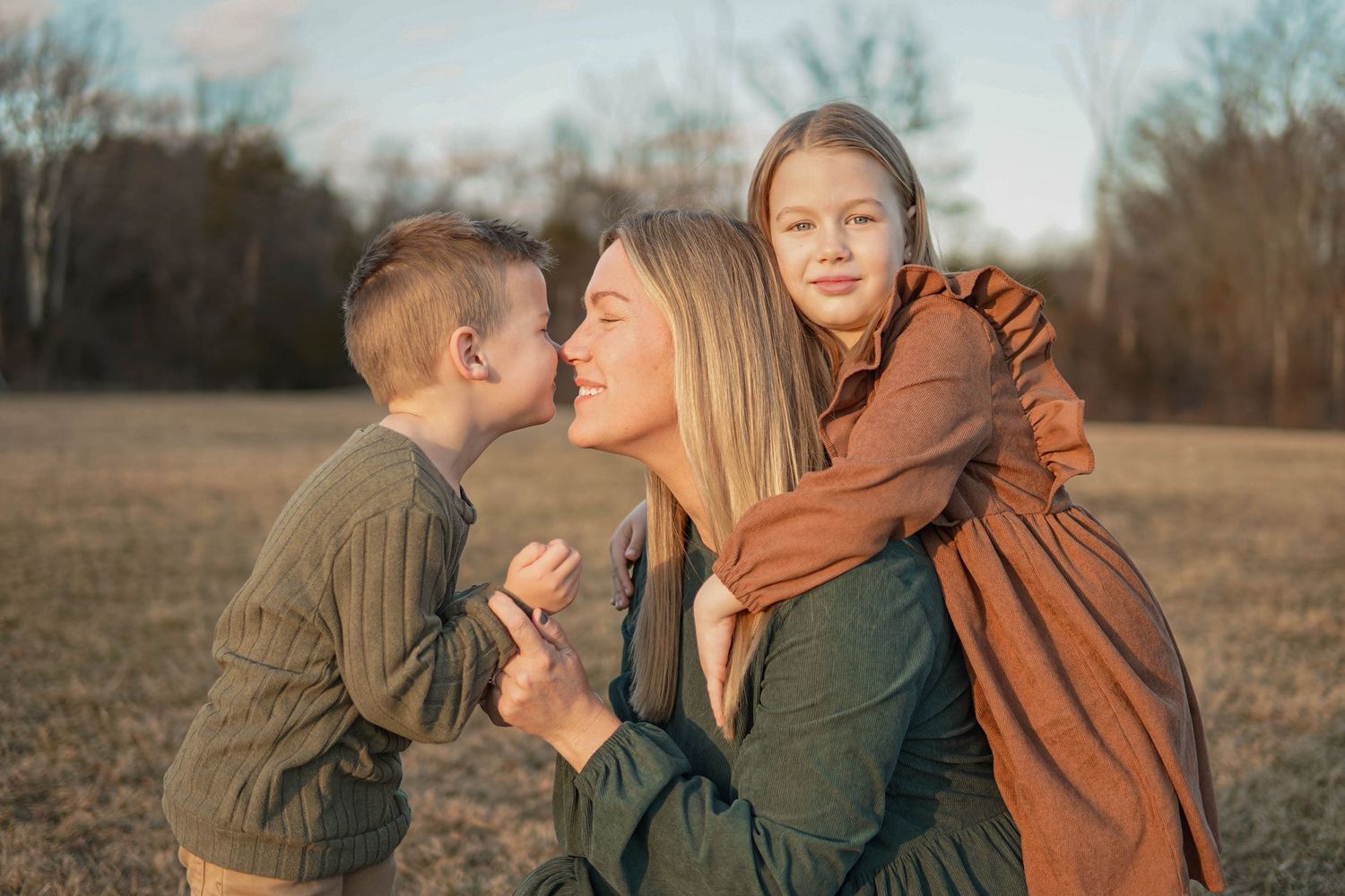 A warm golden-hour family moment captured outdoors in a field during autumn with playful expressions and laughter.