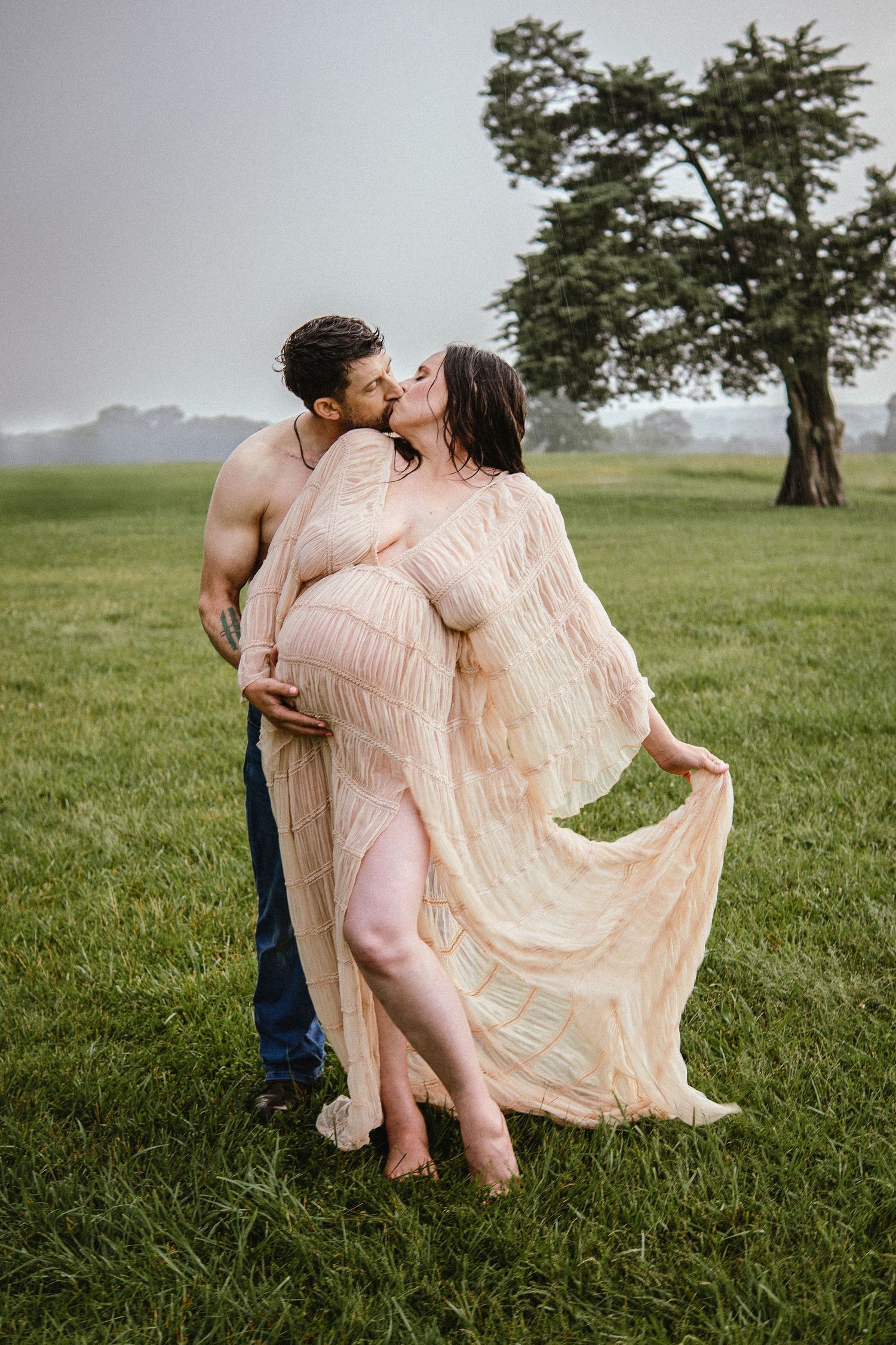 Romantic couple embraces in a grassy field, with her wearing a flowing peach-colored vintage dress.