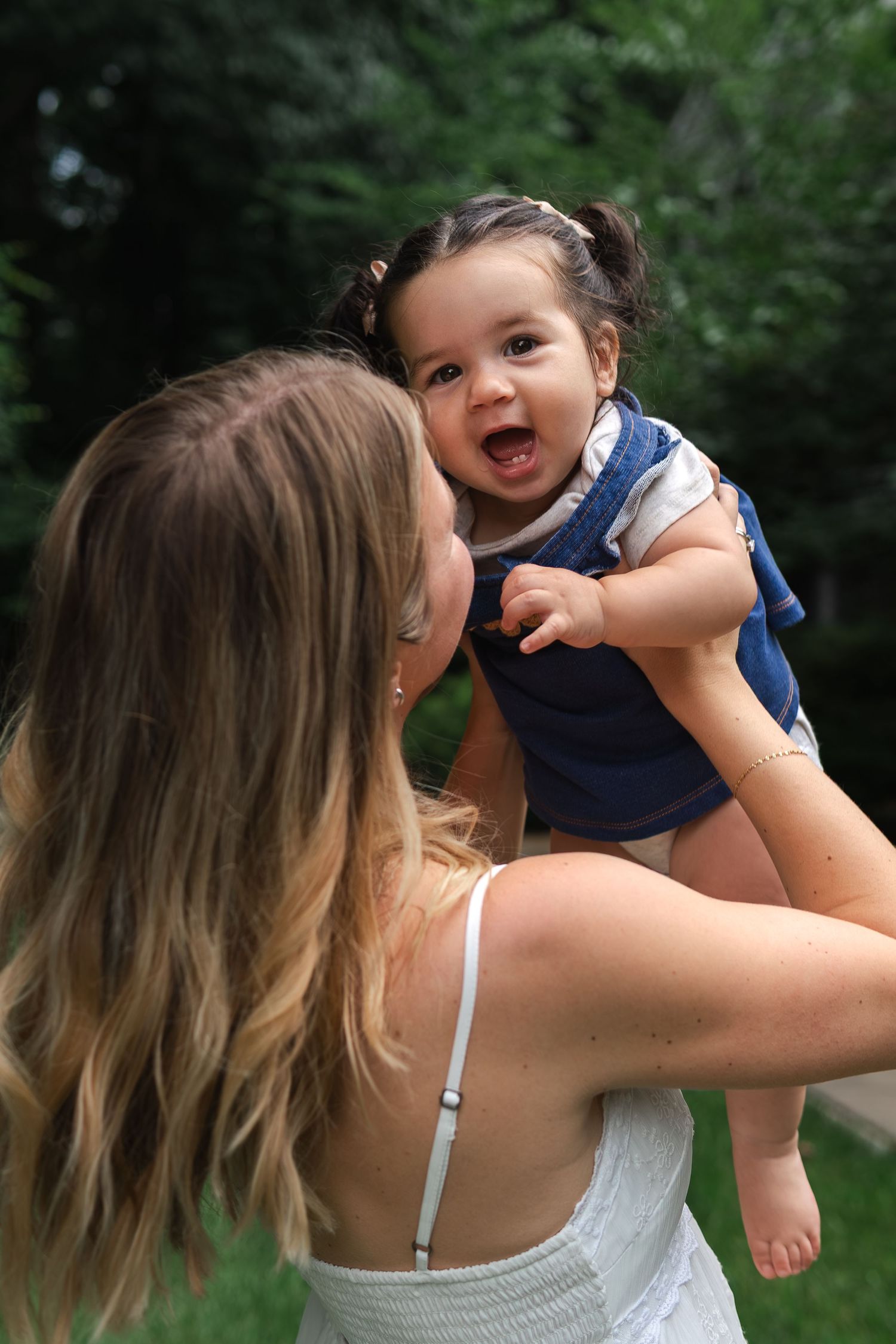 A joyful moment captured outdoors as a baby in blue romper laughs while being lifted up in the summertime.
