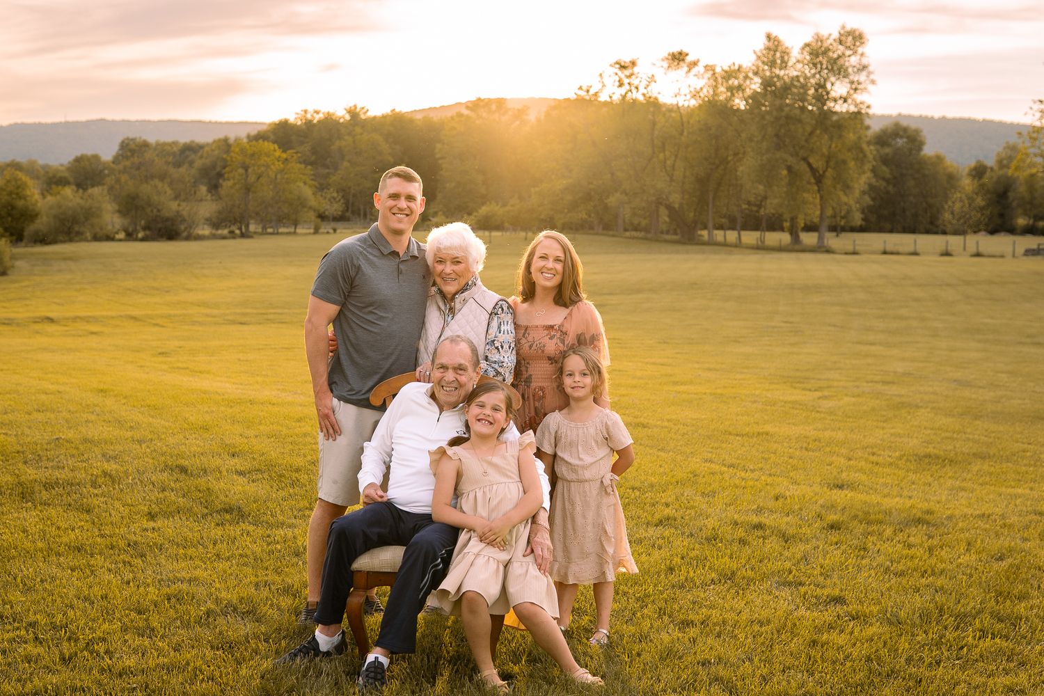 Family gathering outdoors in a golden field during sunset with mountain backdrop and natural lighting.