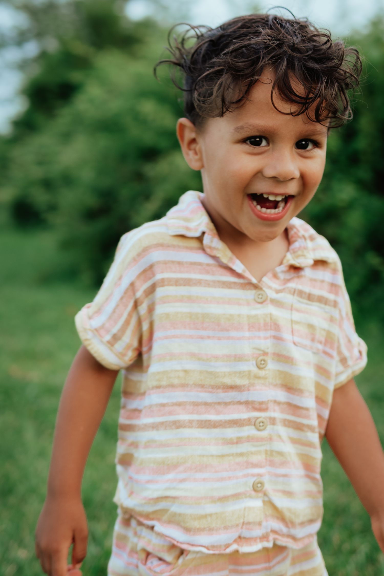 A smiling child in a striped shirt plays outdoors in a grassy field.
