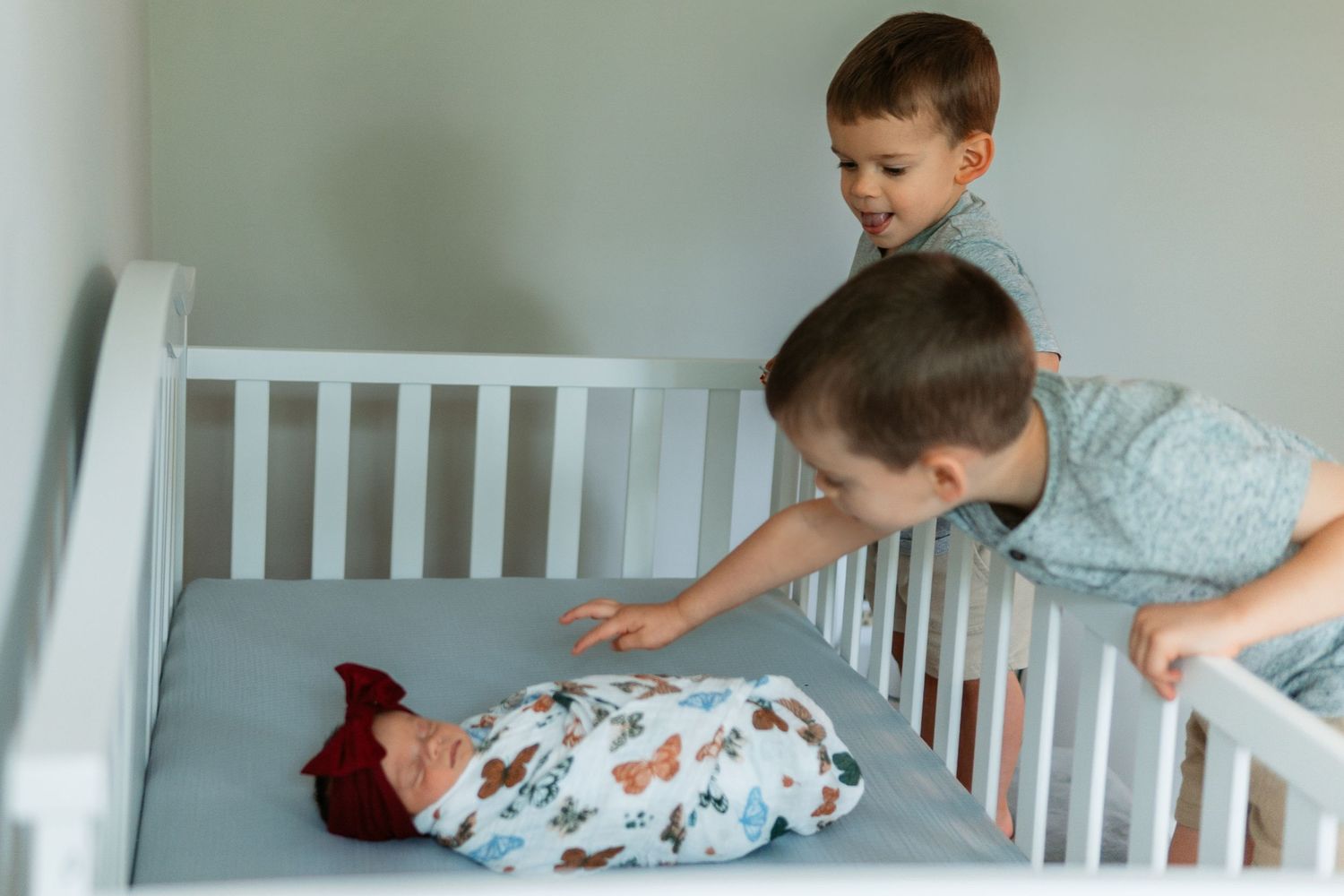 A person leans over the side of a white crib to gently kiss a baby swaddled in a floral blanket.