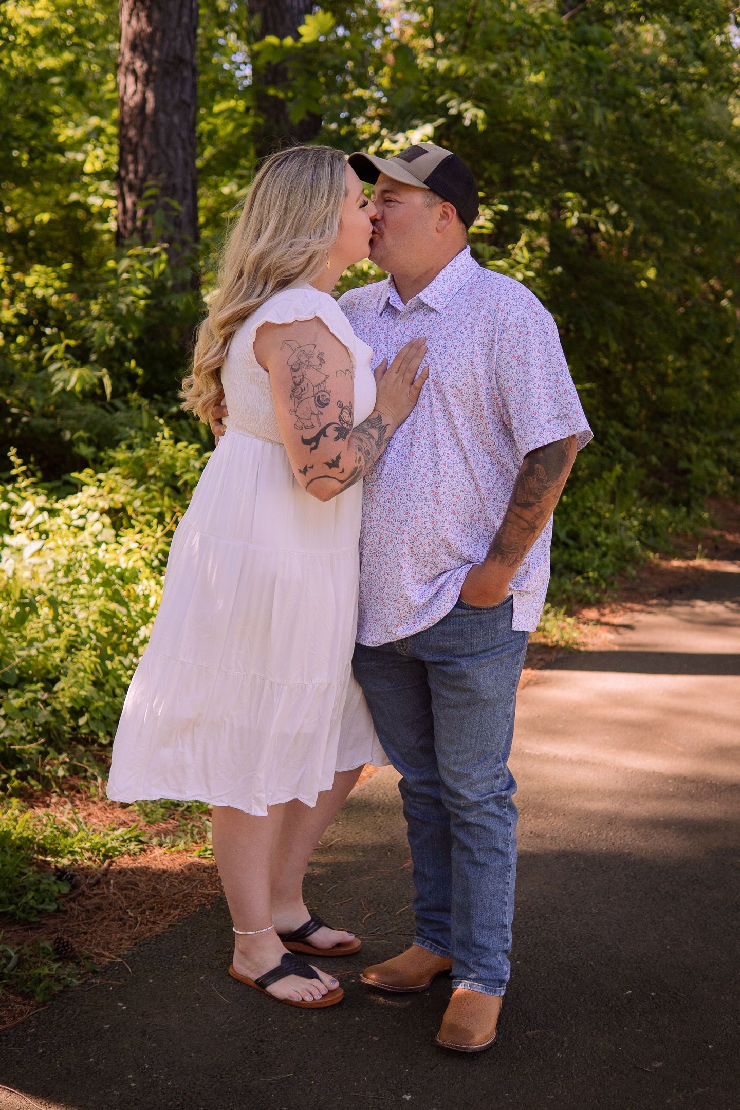 Couple sharing a tender moment on a sunlit path through a wooded area.