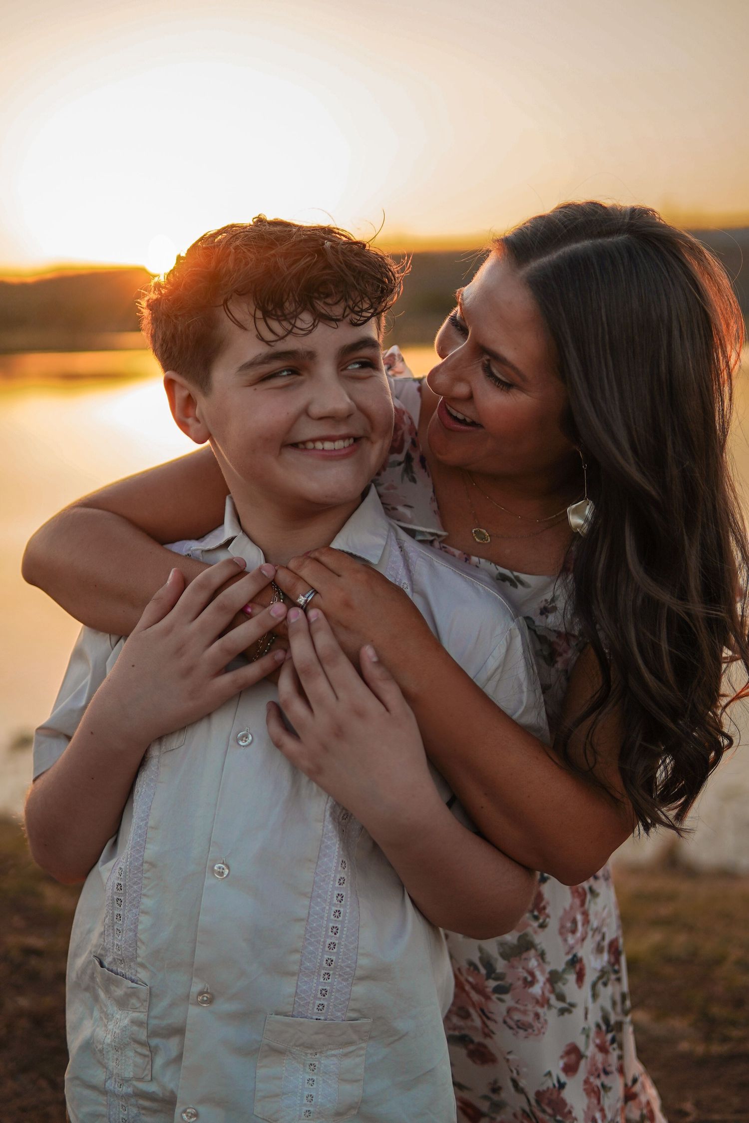Two people embrace and share a joyful moment together during golden hour sunset by the water.