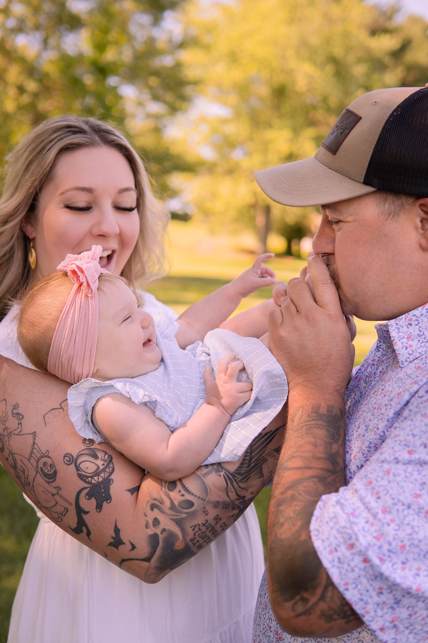 A happy family moment outdoors with a baby and visible tattoo artwork on parent's arm.