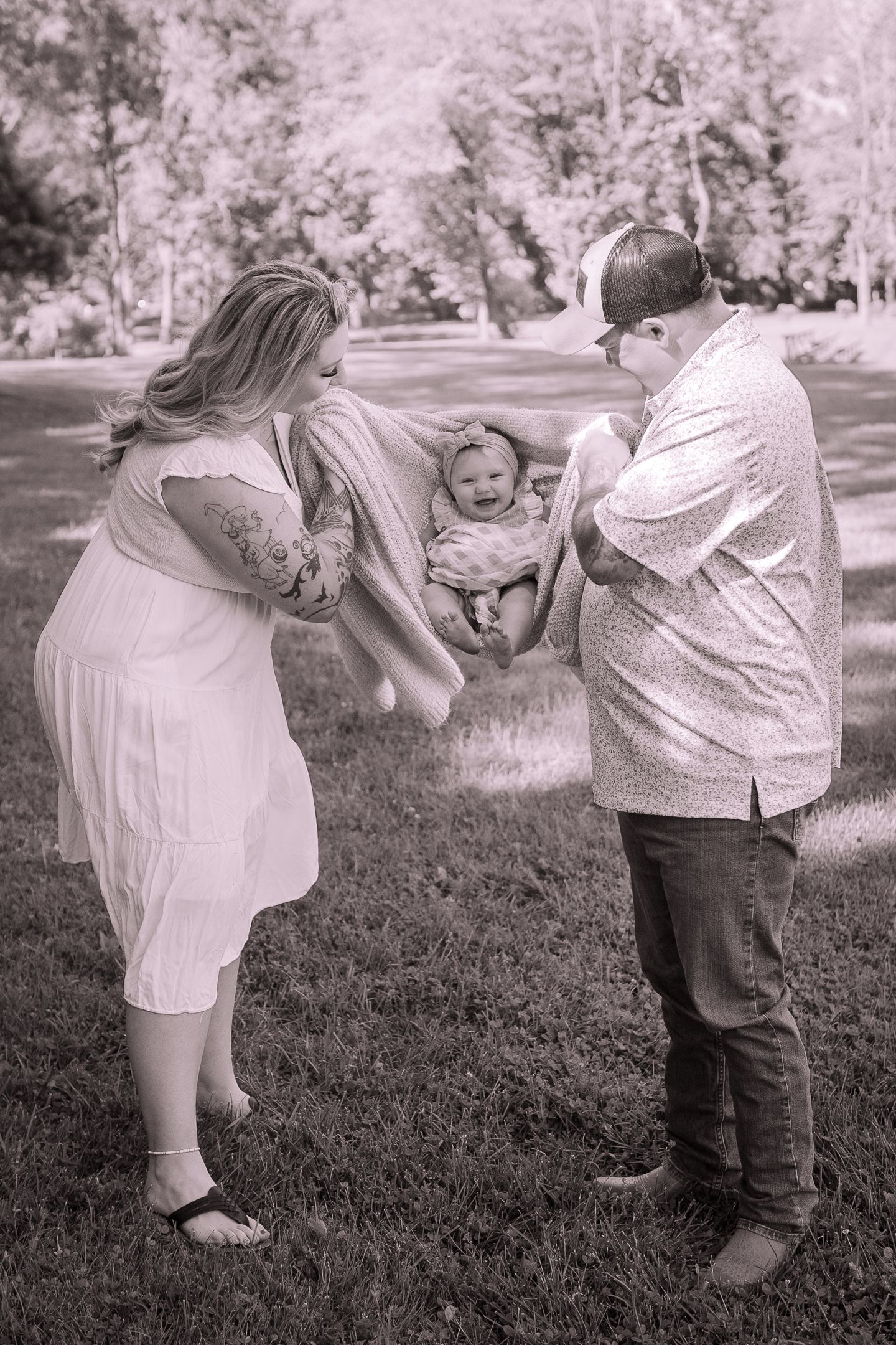 A black and white photo of a family playing with their baby outdoors.