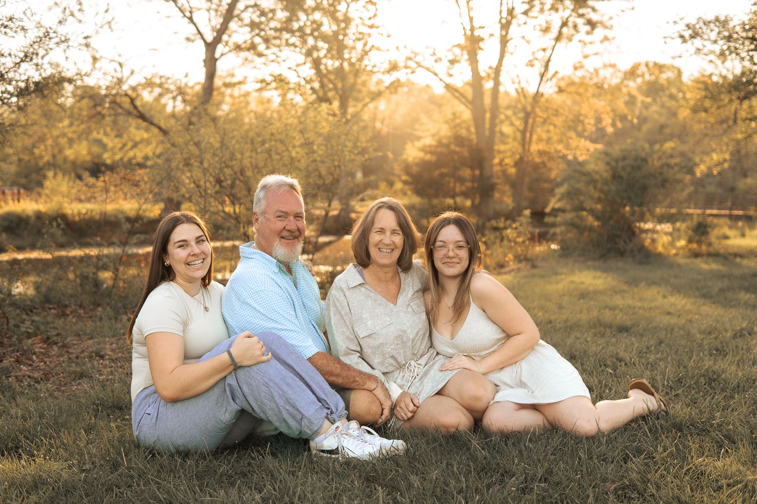 A group sits together on grass in a serene outdoor setting during golden hour with trees in the background in Haymarket, Virginia.