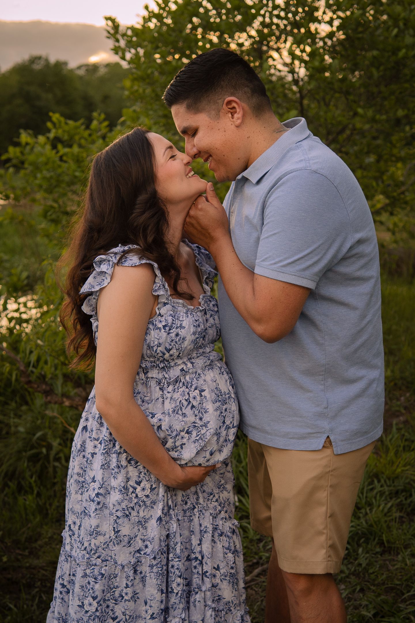 A romantic maternity portrait showing affection between couple in a garden setting at sunset.