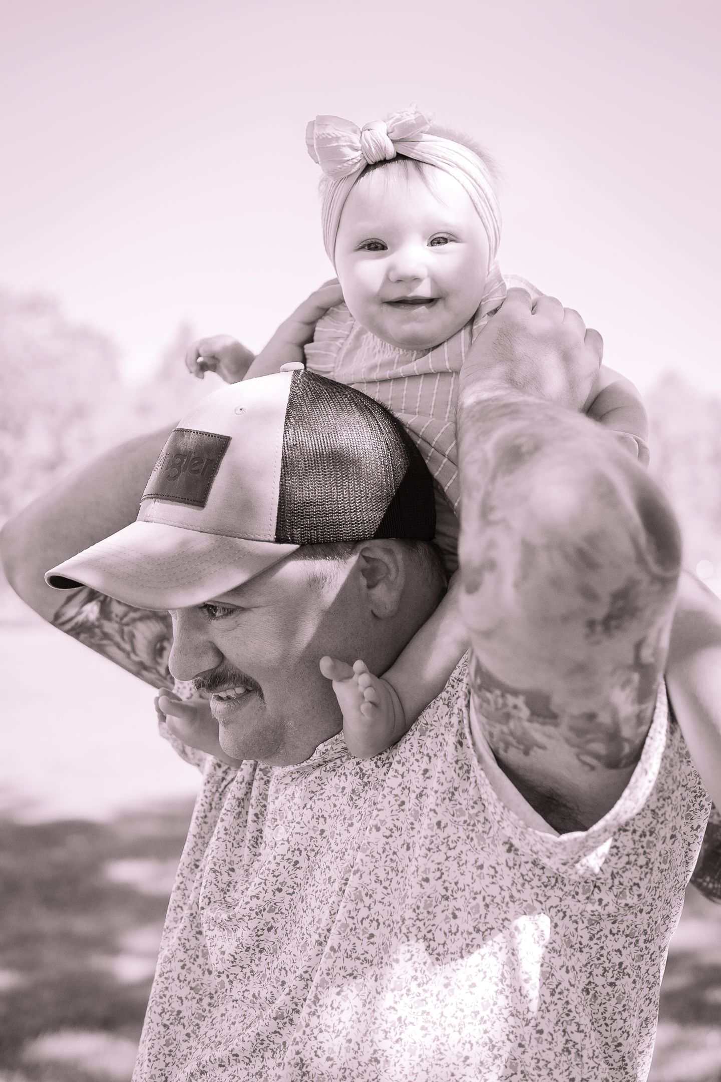 A tender black and white moment showing a baby riding on shoulders and wearing a headband.