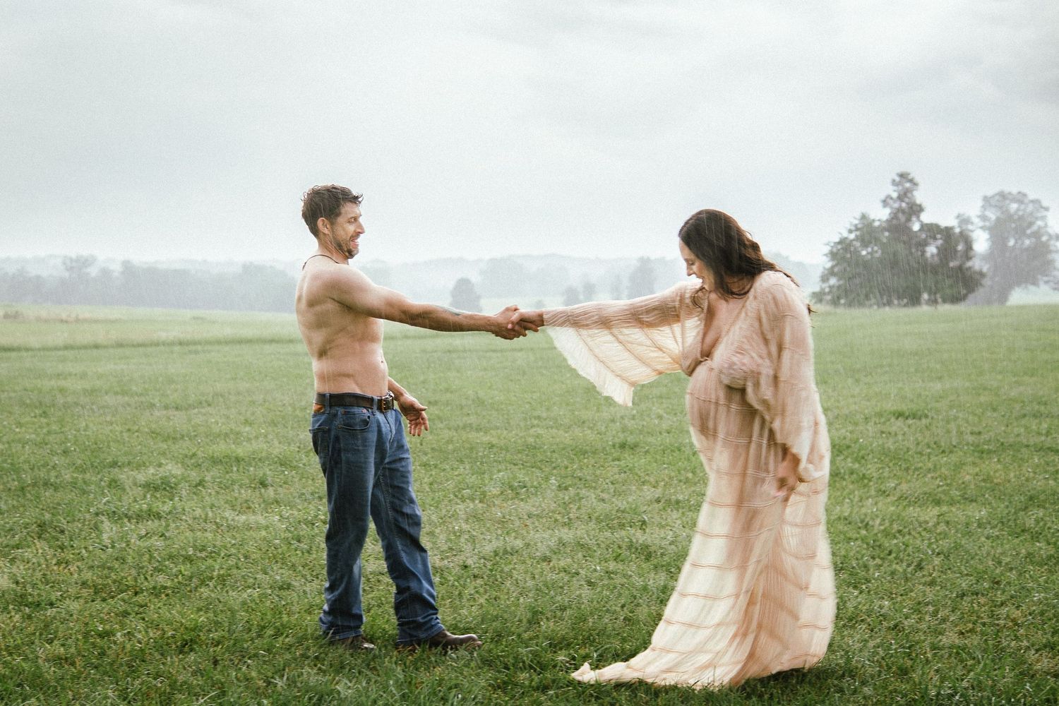 Two figures holding hands walk together in a misty green field on an overcast day.